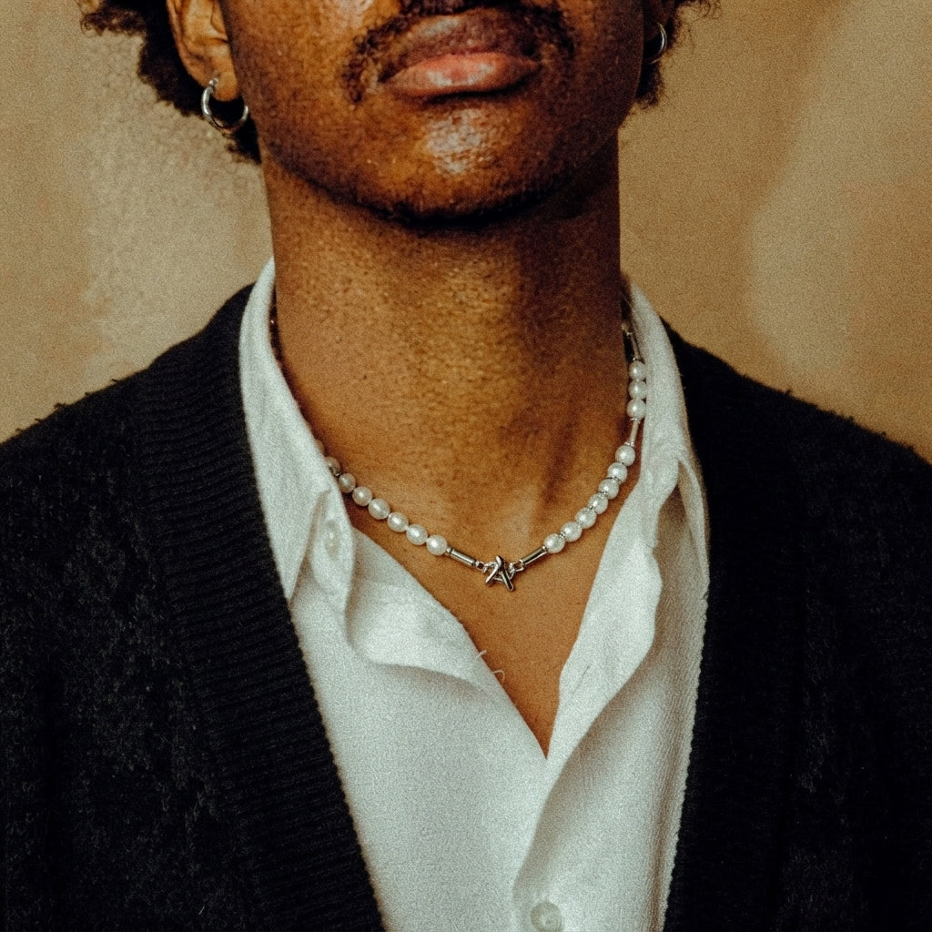 Man wearing a white shirt and black cardigan with a delicate white pearl necklace and silver clasp.