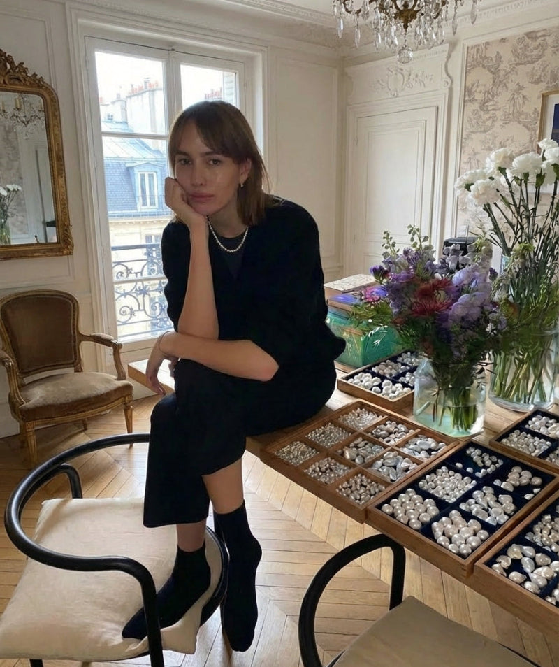 Woman sitting in a stylish room with a table full of jewelry and decorative items.