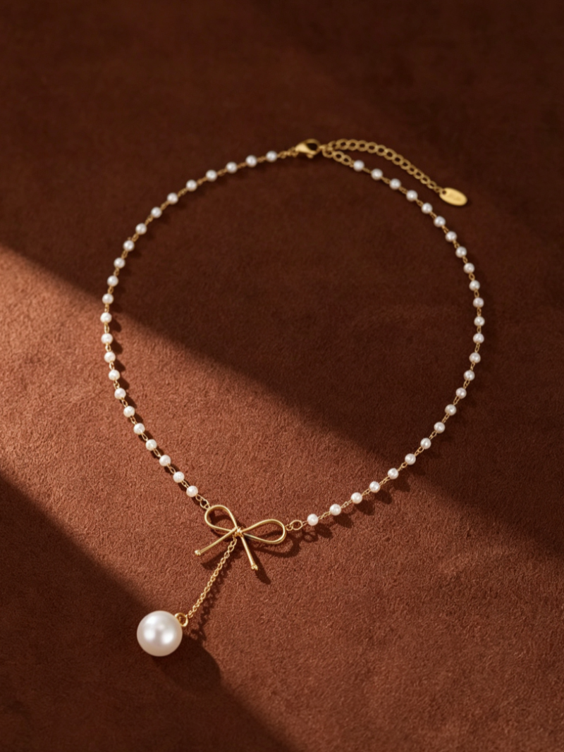 Gold-tone necklace with a delicate chain of small white imitation pearls, featuring a gold bow pendant with a single larger pearl drop.
