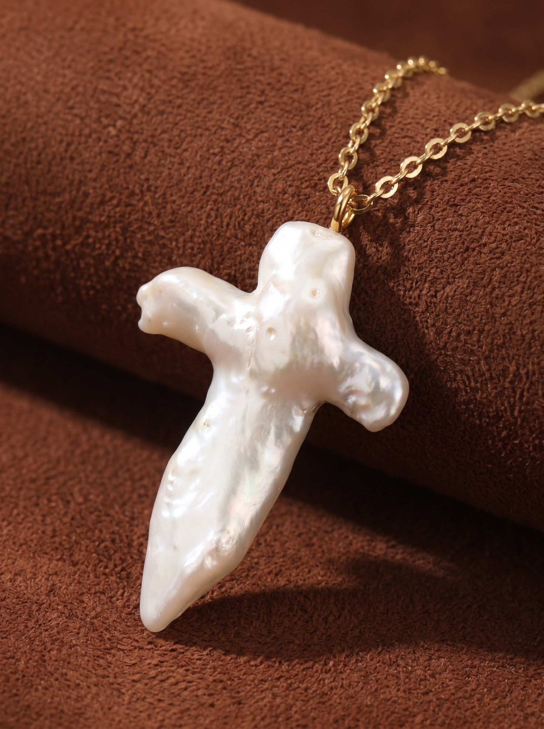 Aegis necklace with a large, irregular white freshwater baroque pearl shaped into a cross, suspended from a gold-toned chain. @pearl