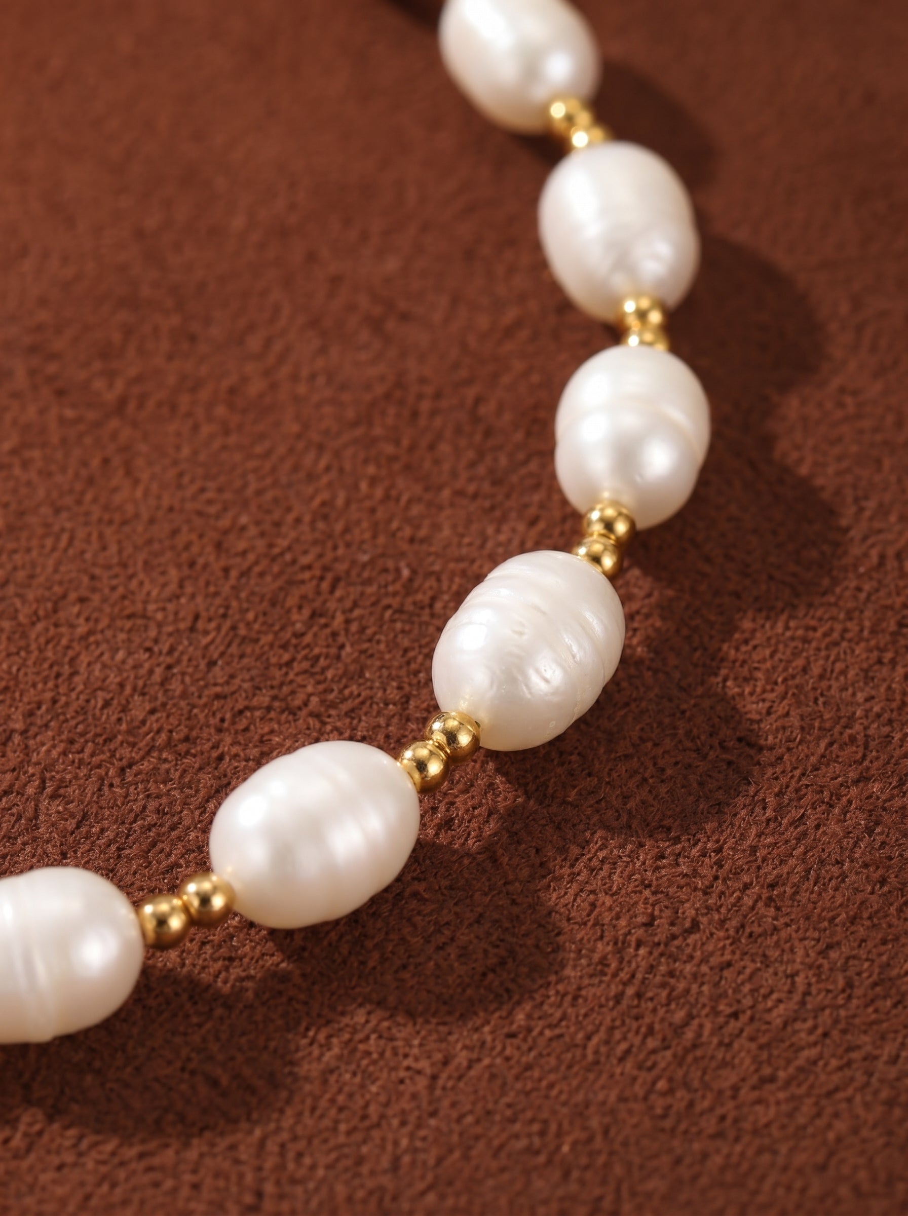 Aetheria freshwater pearl floating chain necklace with evenly spaced oval white seed pearls and gold-toned beads on a brown textured background.@pearl