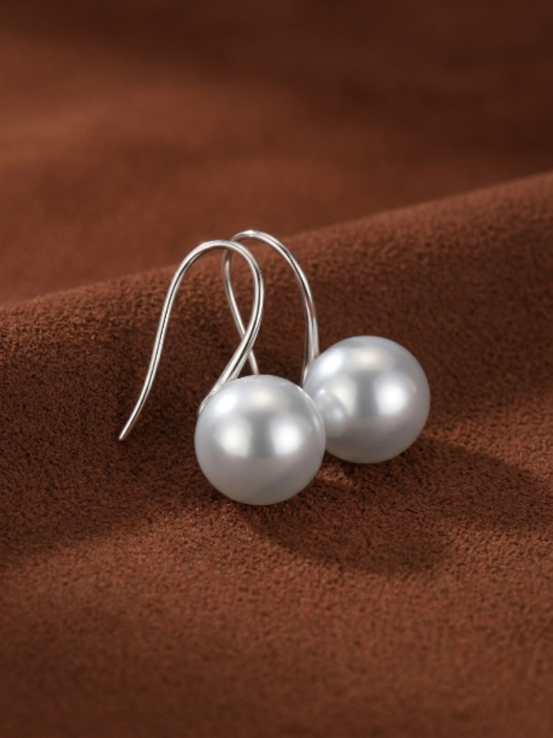 A pair of elegant Alight Akoya Pearl Hoop Earrings with lustrous 9mm white pearls suspended from delicate silver hoops, displayed on a rich brown textured background.
