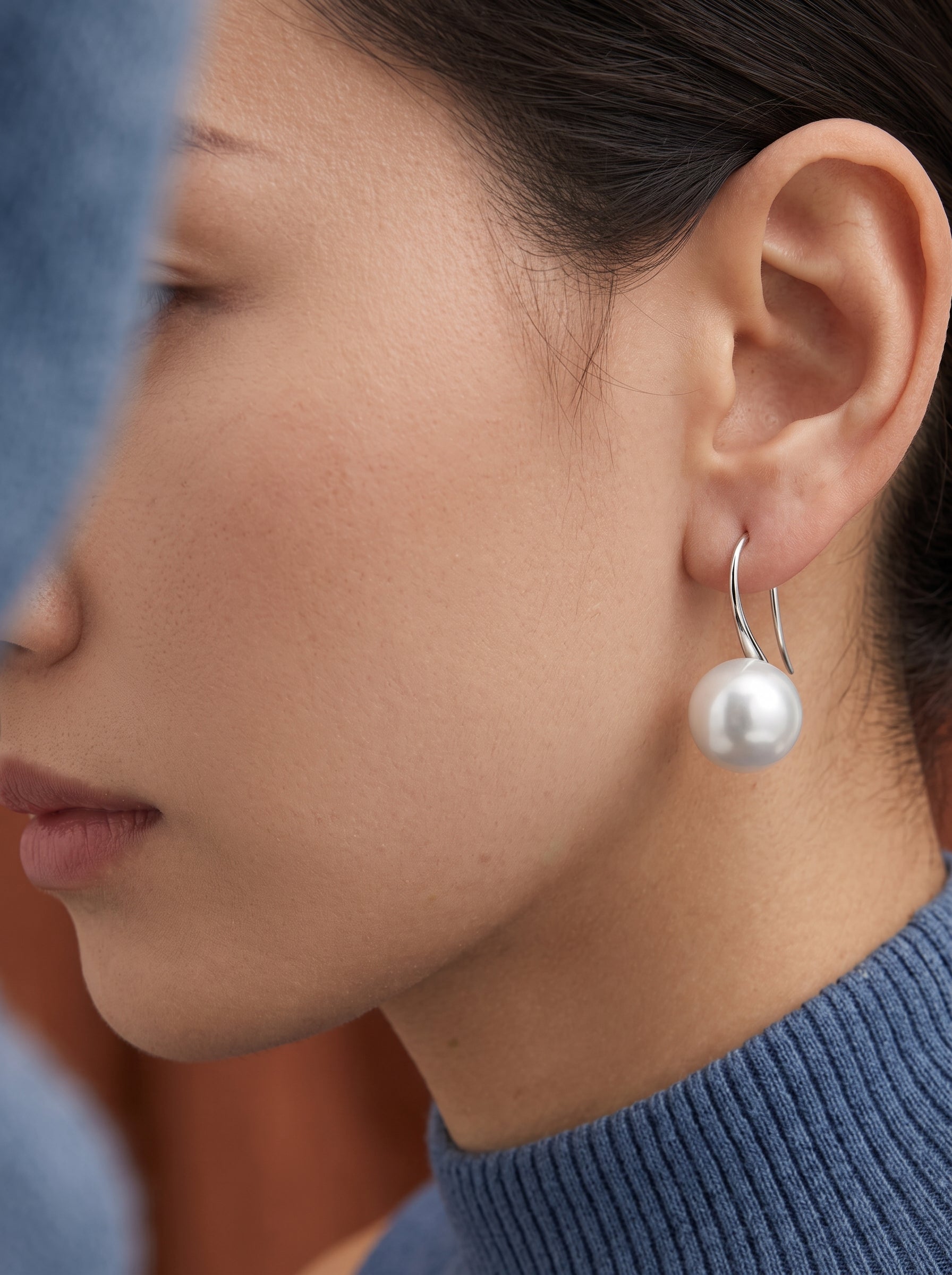 Close-up of a woman wearing Alight Akoya Pearl Hoop Earrings with a single lustrous white pearl dangling from a silver hoop. @model