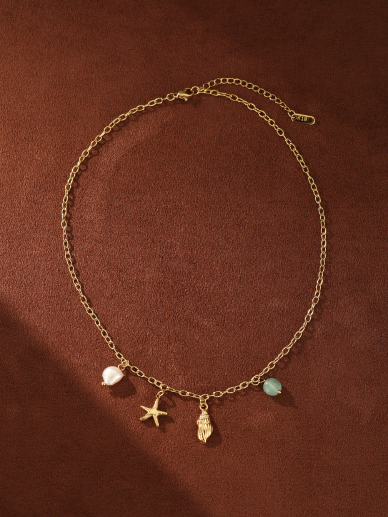 Collier à chaîne dorée présentant une perle d'eau douce, une breloque étoile de mer, une breloque coquillage, et une perle bleu clair, inspiré d'éléments océaniques.
