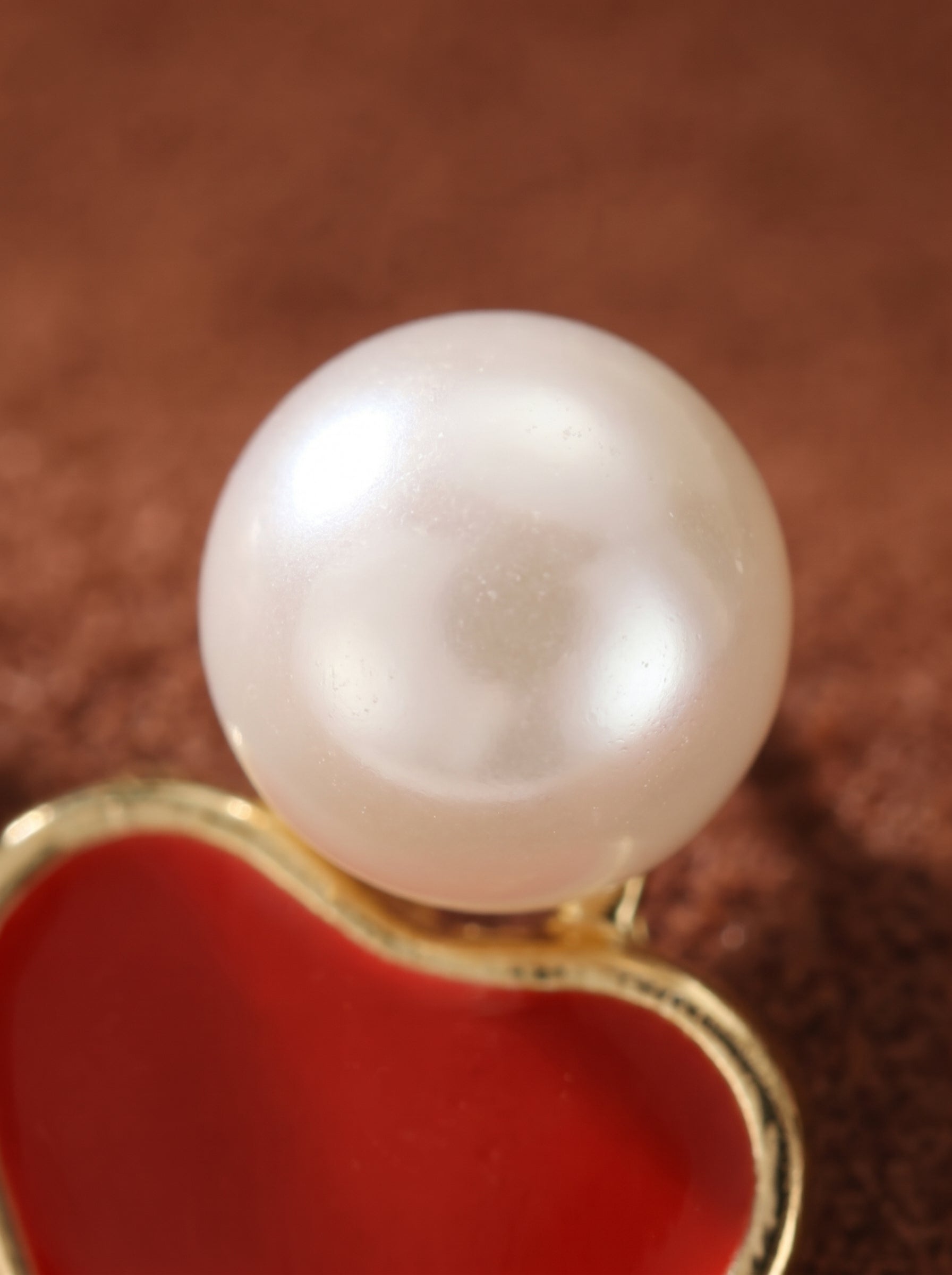 Ardour - Close-up of a white freshwater pearl stud above a red heart-shaped accent on gold-plated drop earrings. @pearl