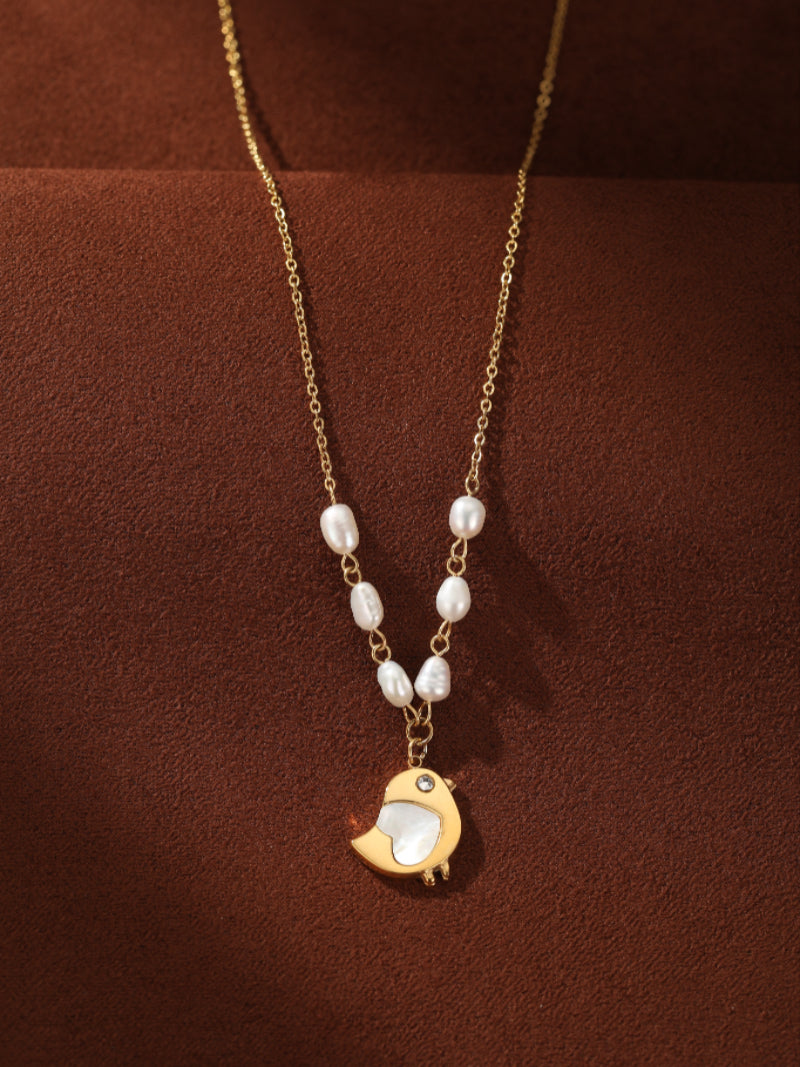 Gold-tone chain necklace featuring a delicate strand of white freshwater seed pearls leading to a charming gold bird pendant with a mother-of-pearl inlay and a small crystal eye.