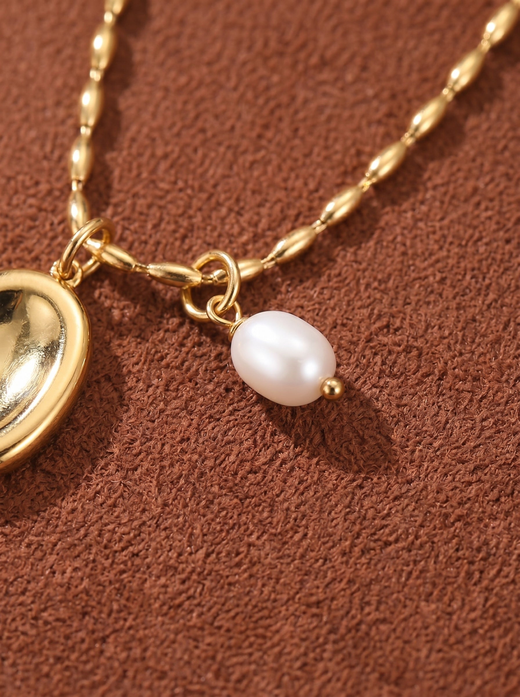 Close-up of a gold chain necklace with a white freshwater pearl and a gold bead accent.@pearl