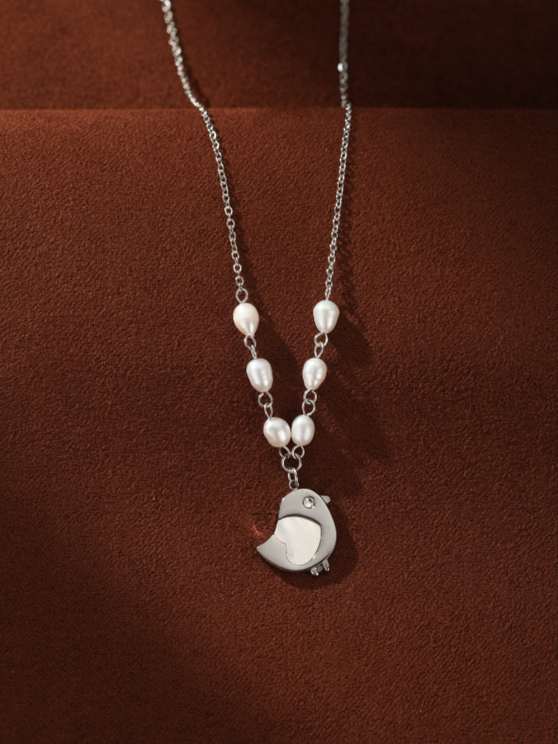 Ascend silver chain necklace featuring a row of white freshwater seed pearls leading to a modern bird pendant with a small gemstone eye. @pearl