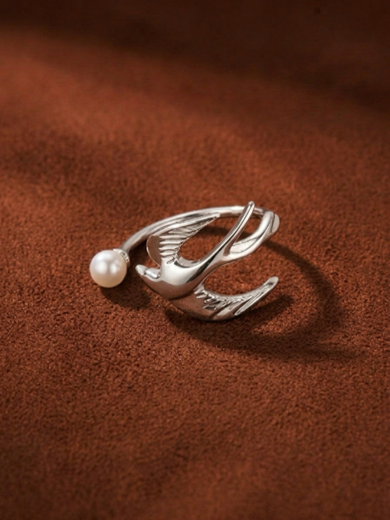 Silver bird cuff ring with a freshwater pearl detail on a brown textured background