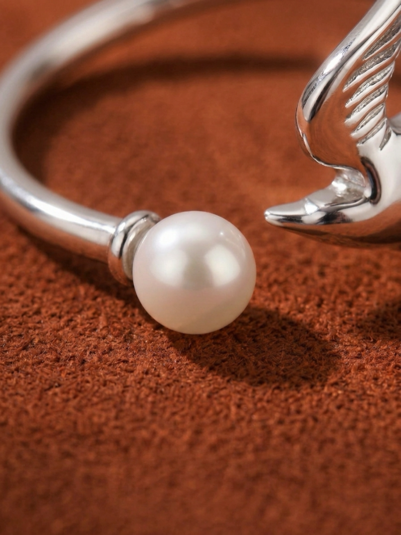 Close-up of a silver cuff ring designed as a bird with wings, holding a luminous freshwater pearl@pearl