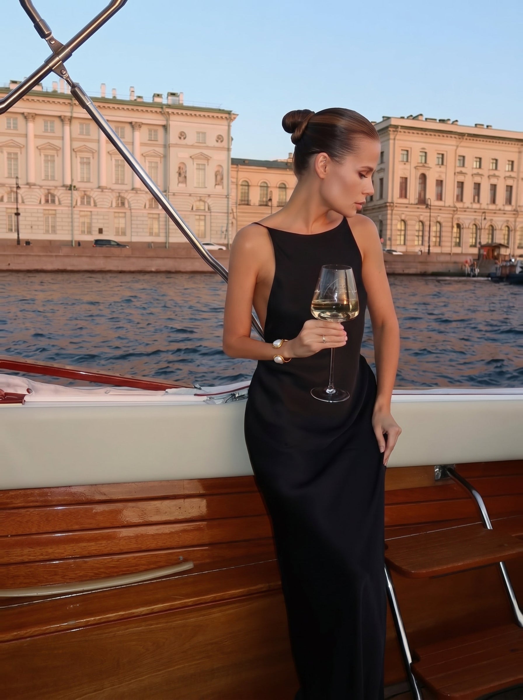 A woman in a black dress on a boat, holding a glass of white wine and wearing Aura Freshwater Pearl Cuff Bracelets with two large baroque pearls on a gold open cuff. @lifestyle #lifestyle