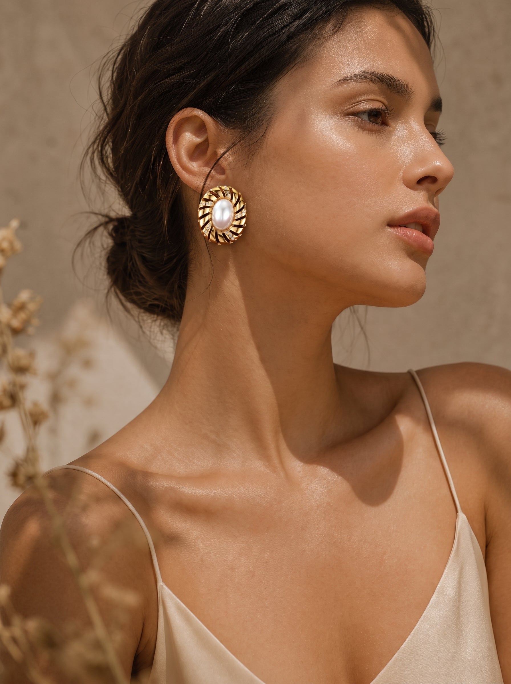 Close-up of a woman wearing Aurelian freshwater baroque pearl stud earrings with a gold-toned sculptural spiral setting. @model