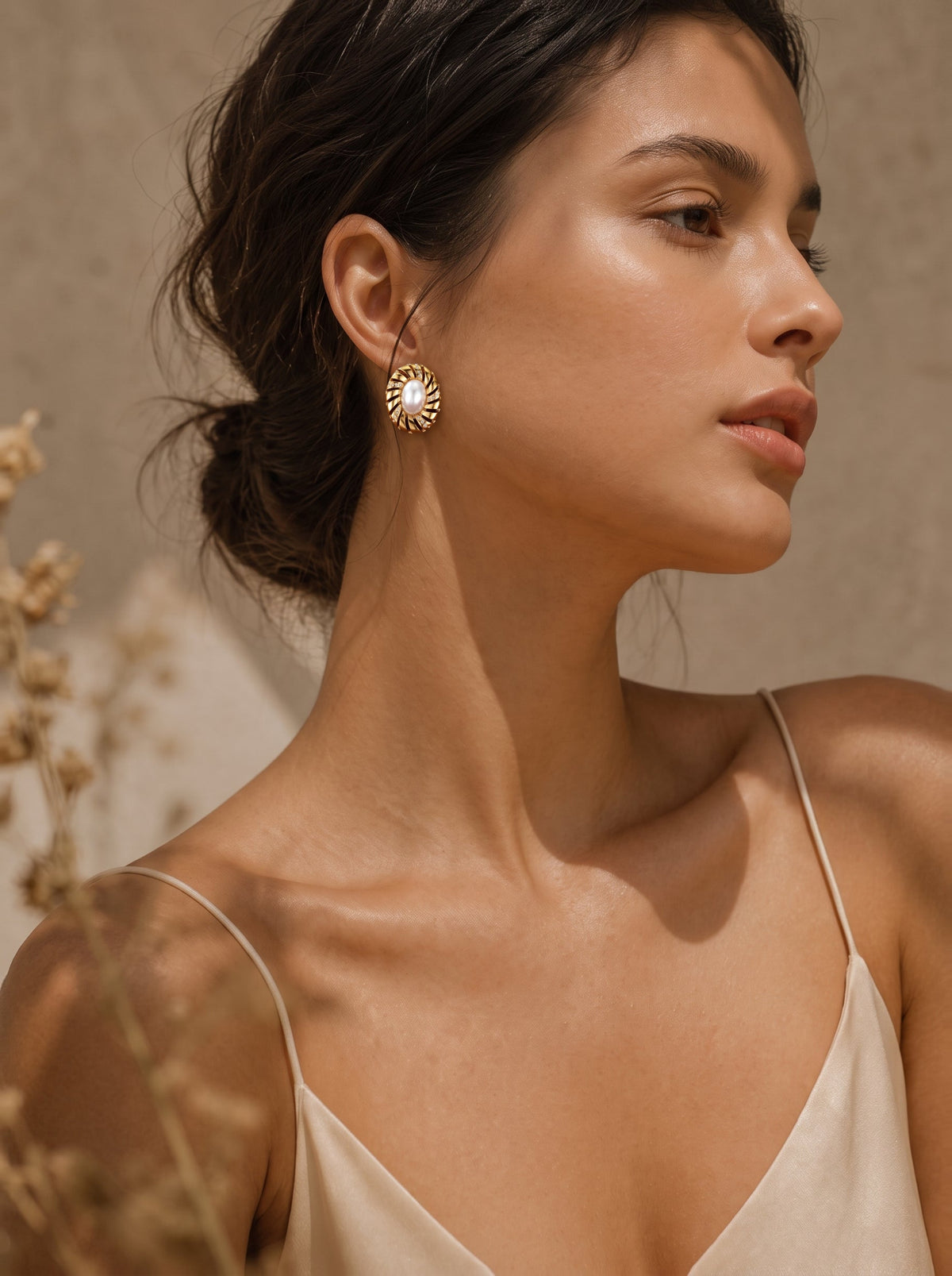 Gros plan d'une femme portant les boucles d'oreilles puces Aurelian en perle baroque d'eau douce avec une monture spiralée sculpturale ton or. @model