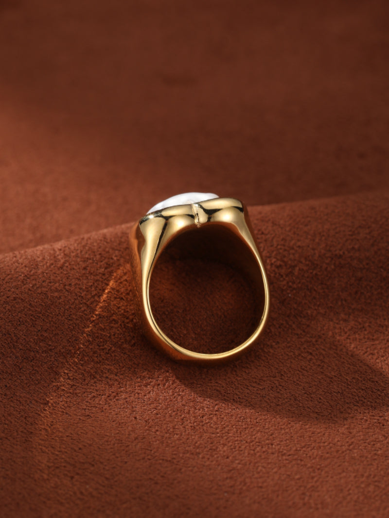 Bold Embrace gold-tone cuff ring featuring a heart-shaped bezel set with a white Baroque freshwater pearl, shown on a brown textured surface. @pearl