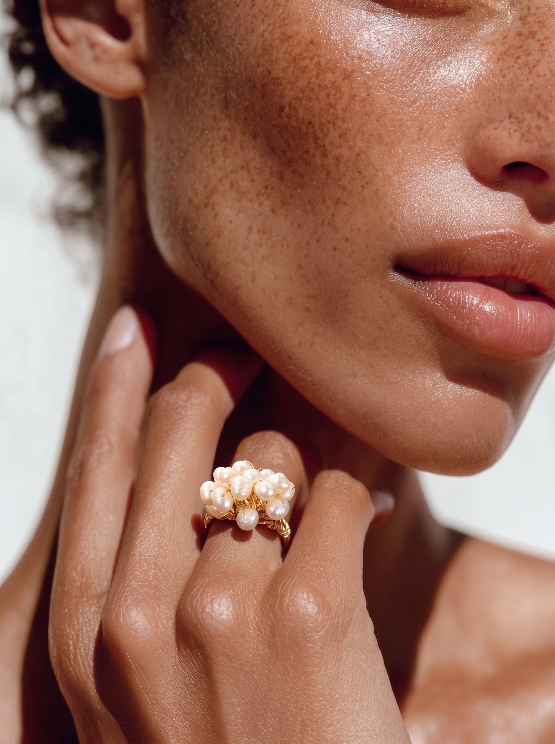 Close-up of a woman's hand wearing the Caprice Freshwater Pearl Beaded Ring, featuring a cluster of small, irregular white pearls on a gold-toned wire band. @model