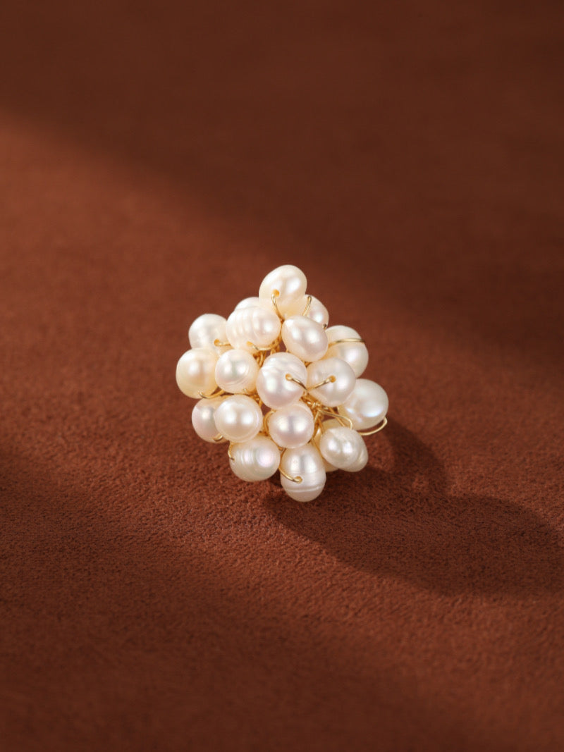 Caprice Freshwater Pearl Beaded Ring featuring a cluster of irregular white Baroque pearls wired together on a gold-tone band, set against a textured brown background.