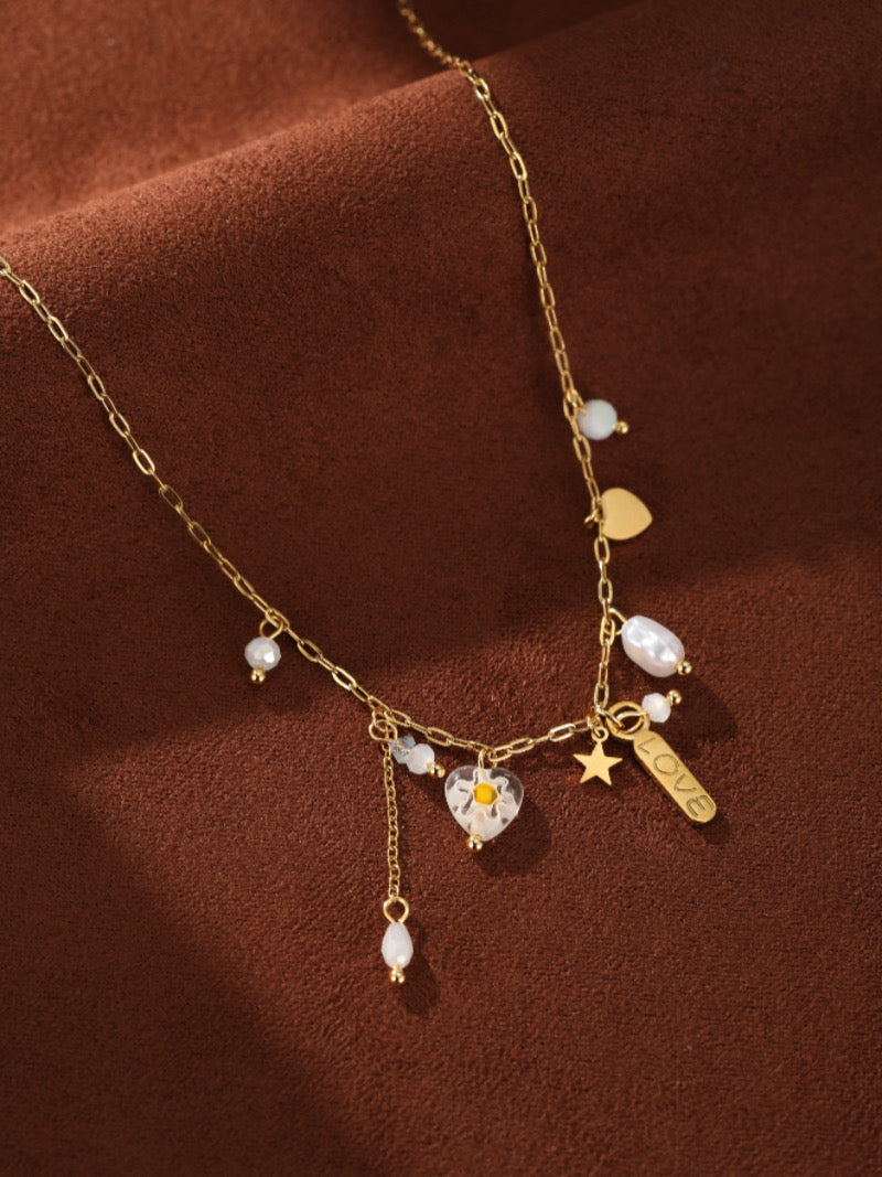 Gold-tone necklace with freshwater pearls, a star charm, a heart charm with a flower inside, and a 'LOVE' tag.