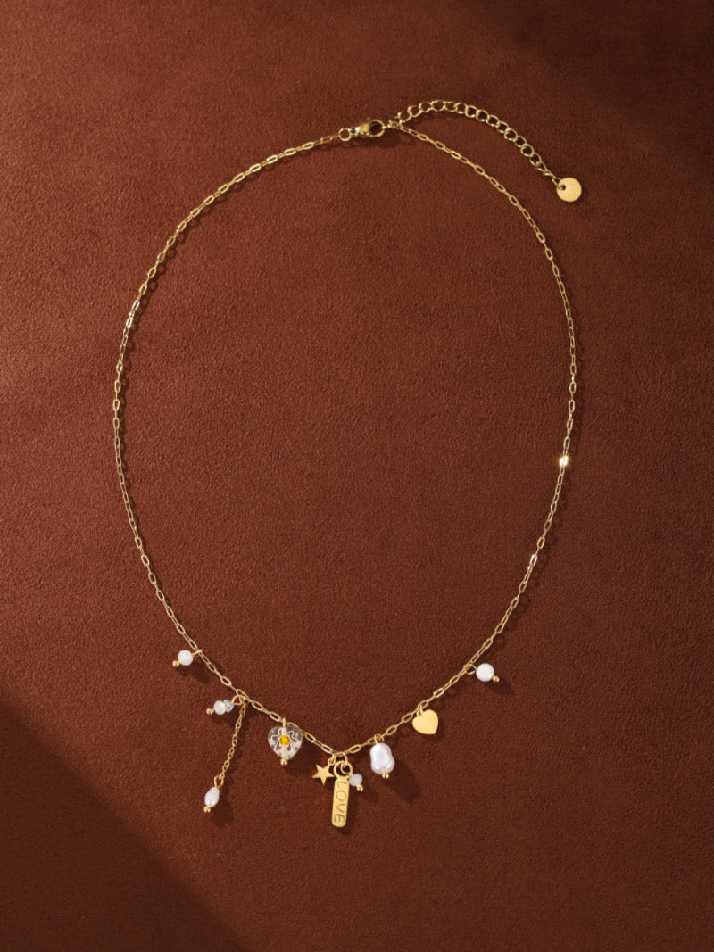A delicate gold-tone necklace featuring a thin chain with scattered freshwater pearls and charms including a star, a heart, and a 'LOVE' tag.