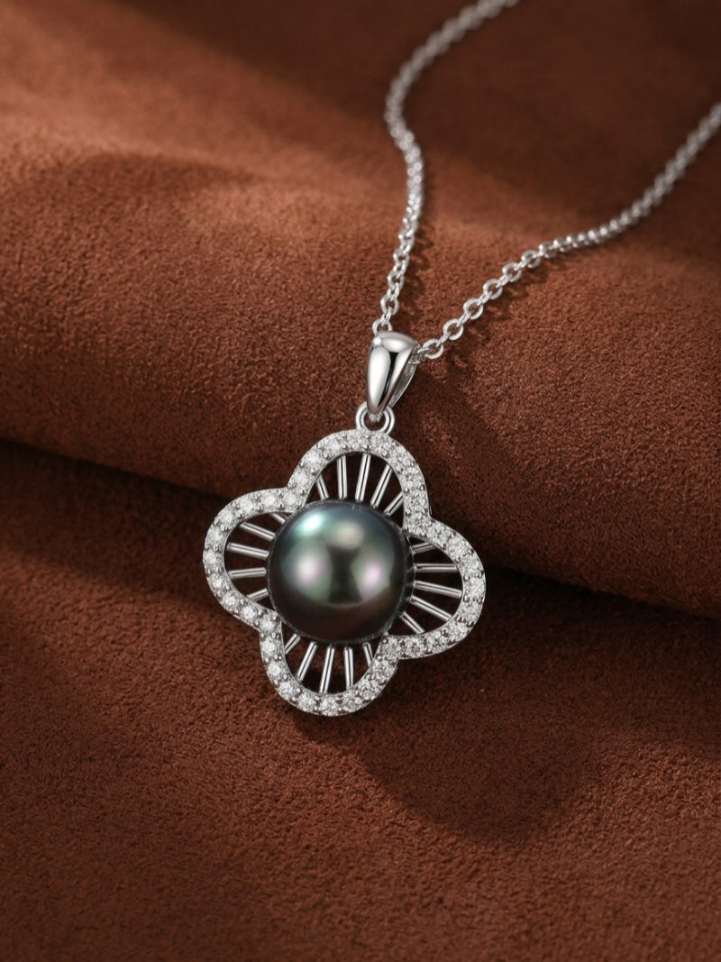 A single pendant necklace featuring a black Tahitian Mabe pearl set in a quatrefoil design surrounded by small accent stones, on a silver chain against a brown textured background.
