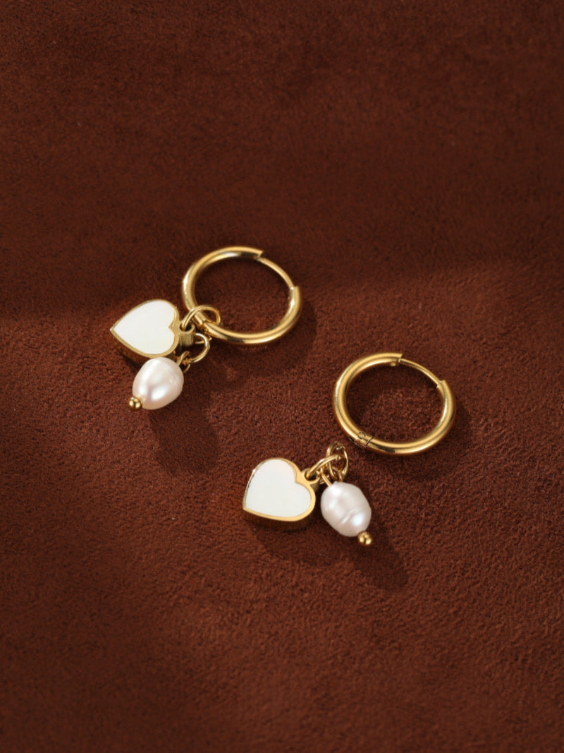 Paire de boucles d'oreilles goutte créoles ton or présentant des breloques cœur en émail blanc et des perles graines d'eau douce.