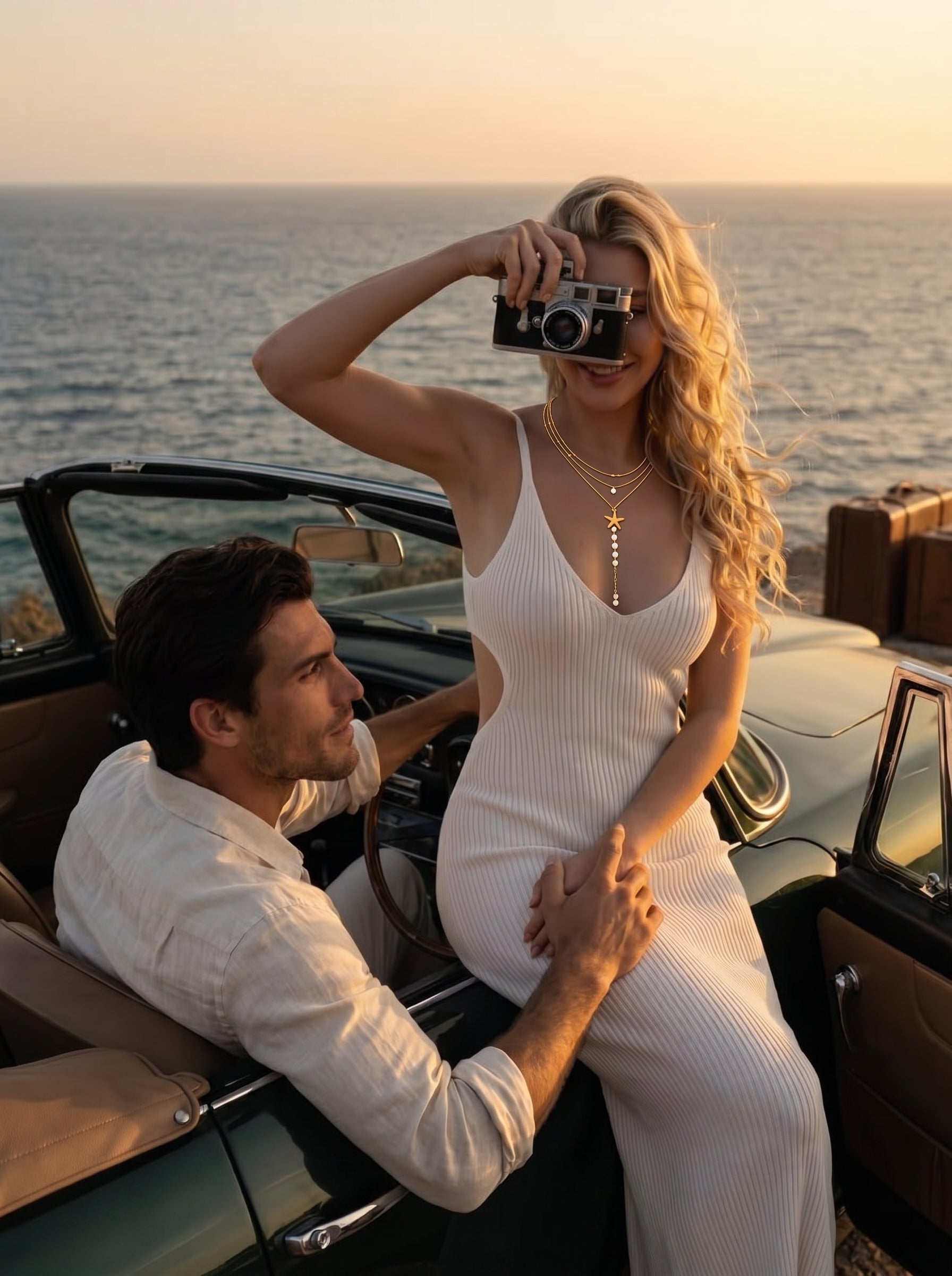 Une femme en robe blanche et un collier doré superposé avec une breloque étoile de mer et des perles d'eau douce, tenant un appareil photo vintage, assise dans une décapotable à côté d'un homme, avec l'océan et le coucher de soleil en arrière-plan. @lifestyle