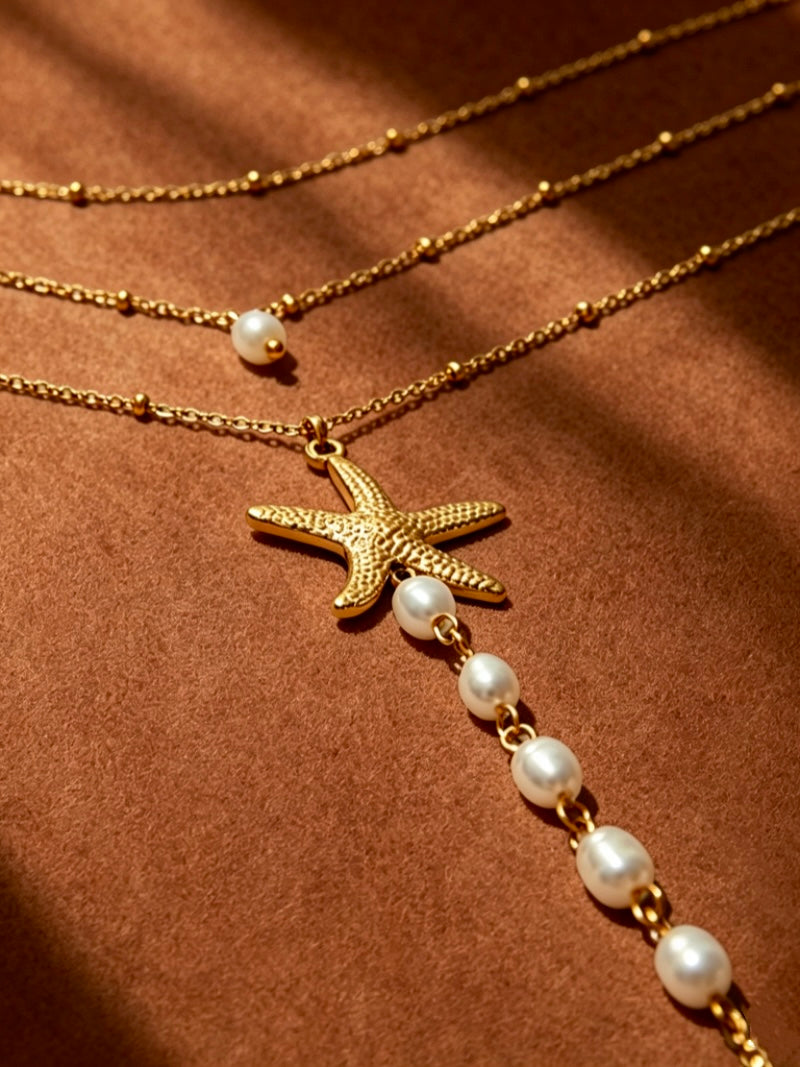 Close-up of a layered gold necklace featuring a textured starfish charm and a strand of white freshwater pearls.