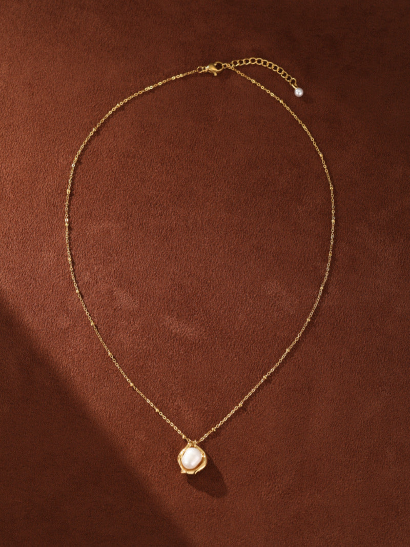 Collier à chaîne perlée ton or présentant une perle blanche d'eau douce sertie dans un pendentif vase organique et sculptural.