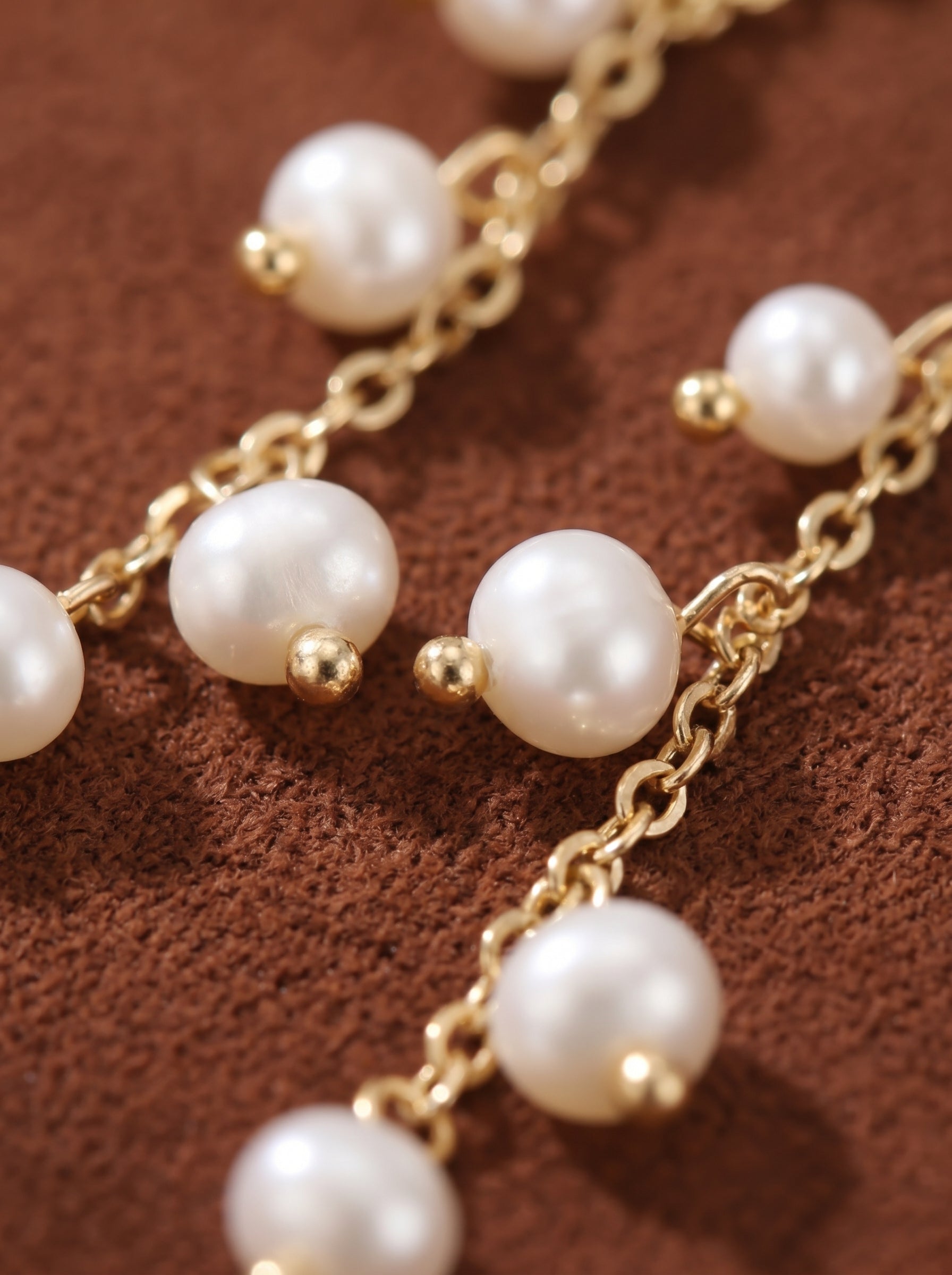 Close-up of elegant gold chain drop earrings featuring multiple lustrous white freshwater pearls, each accented with a tiny gold bead.@pearl