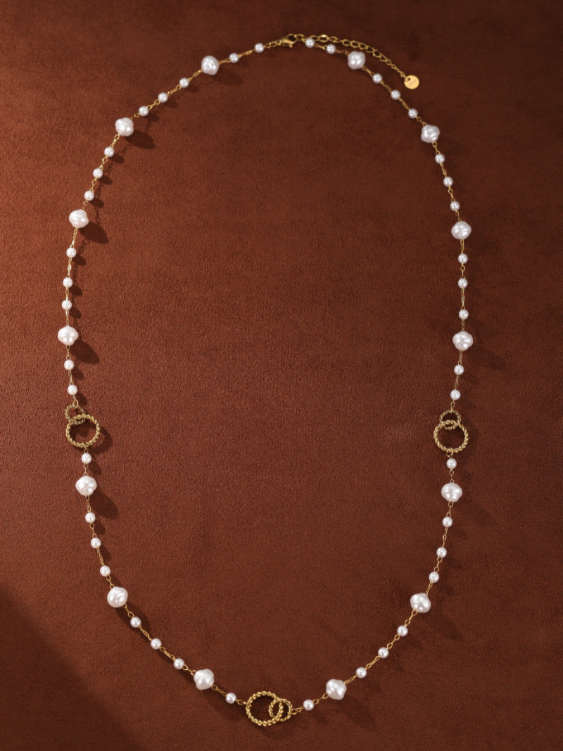 A long, gold-tone necklace featuring a delicate chain adorned with varying sizes of white imitation baroque pearls and textured gold-tone rings.