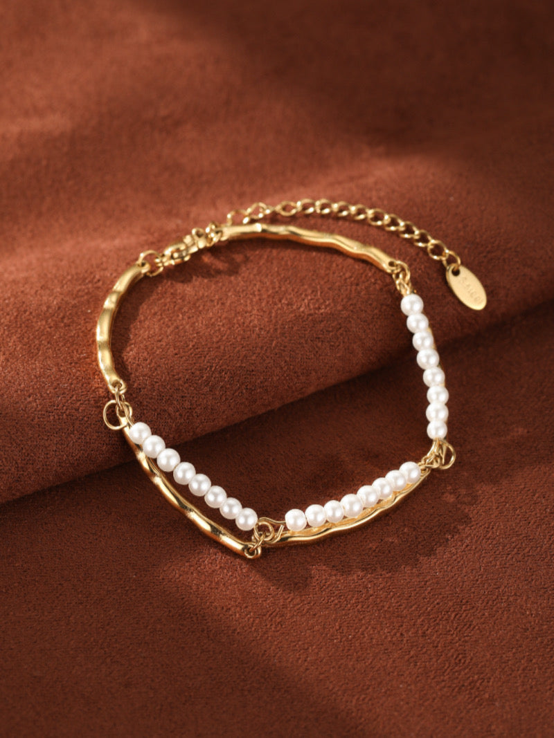 Gold-tone curved chain bracelet featuring two rows of delicate 3.5mm freshwater pearls on a brown background.