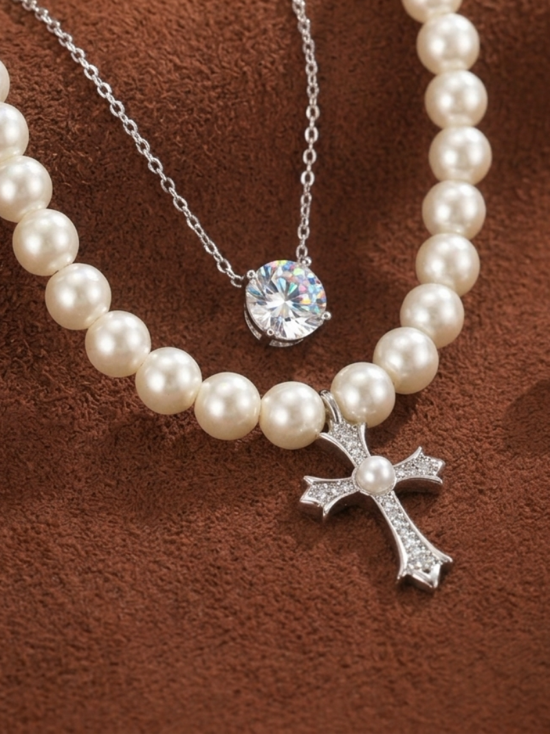 Covenant layered necklace featuring a strand of white imitation pearls with a diamond-encrusted cross pendant and a separate delicate silver chain with a solitaire gemstone.