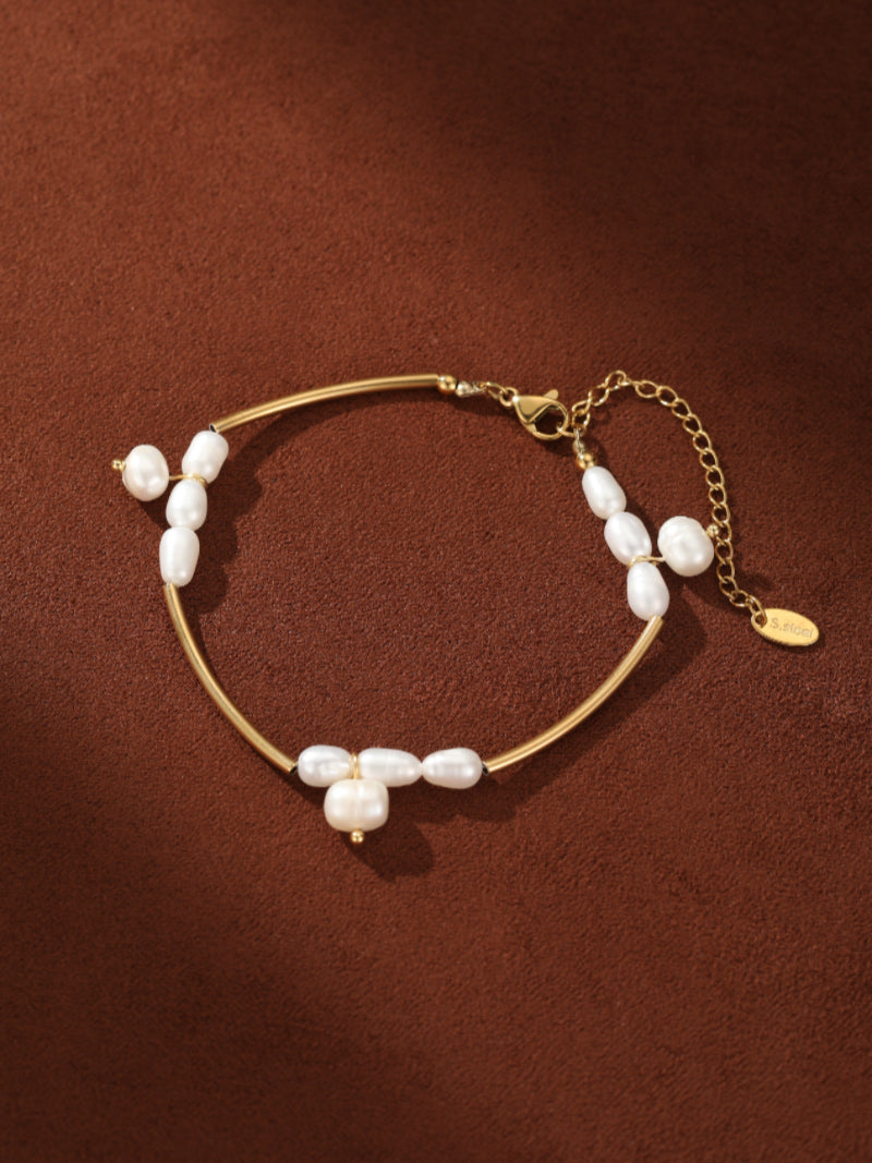 Gold-toned chain bracelet with white seed-shaped freshwater pearls arranged asymmetrically on a curved bar, featuring an adjustable clasp.