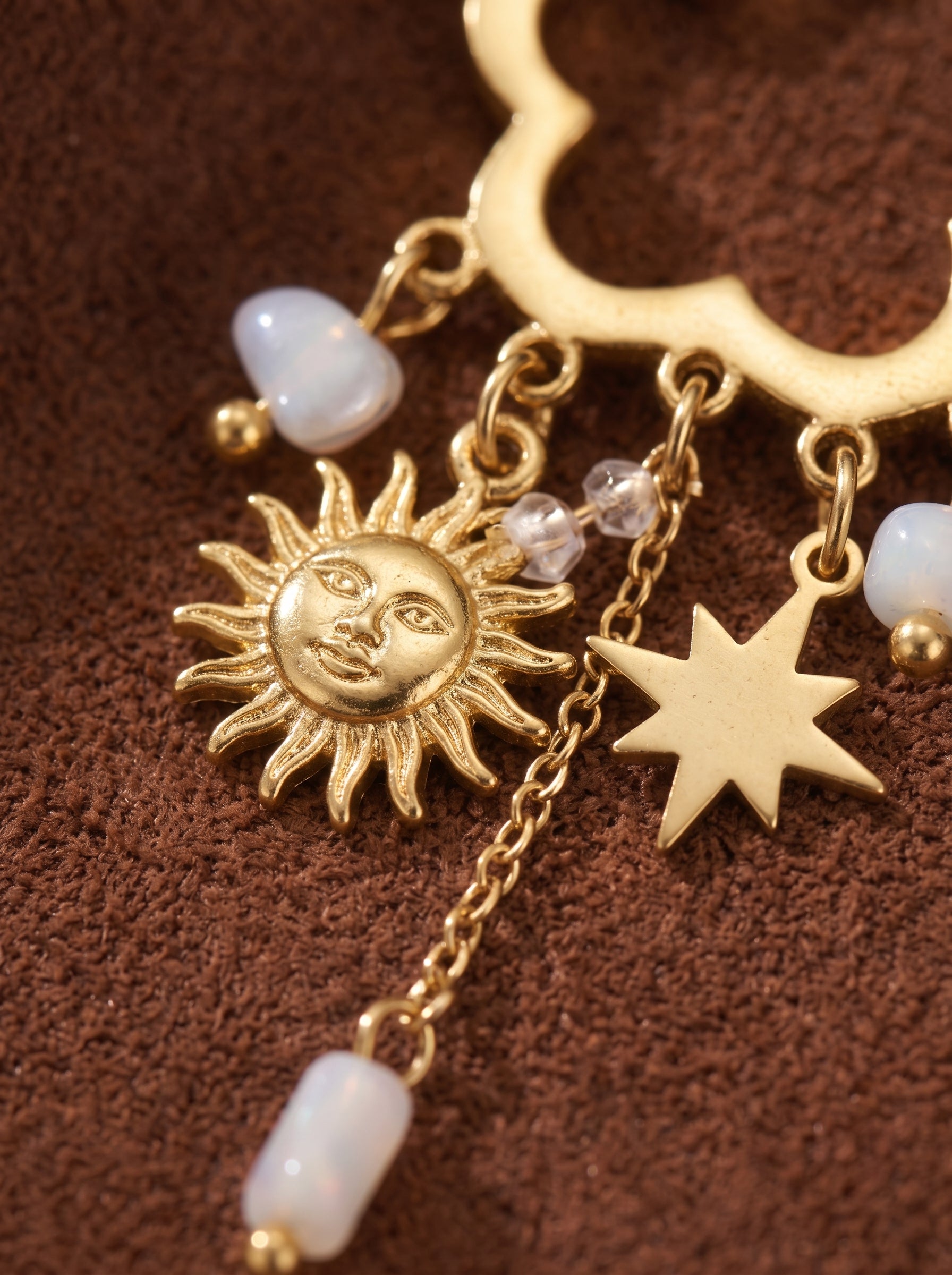 Gros plan des boucles d'oreilles Daydream présentant une breloque soleil ton or avec un visage, une breloque étoile ton or, et des perles graines blanches d'eau douce pendant d'une chaîne ton or. @pearl