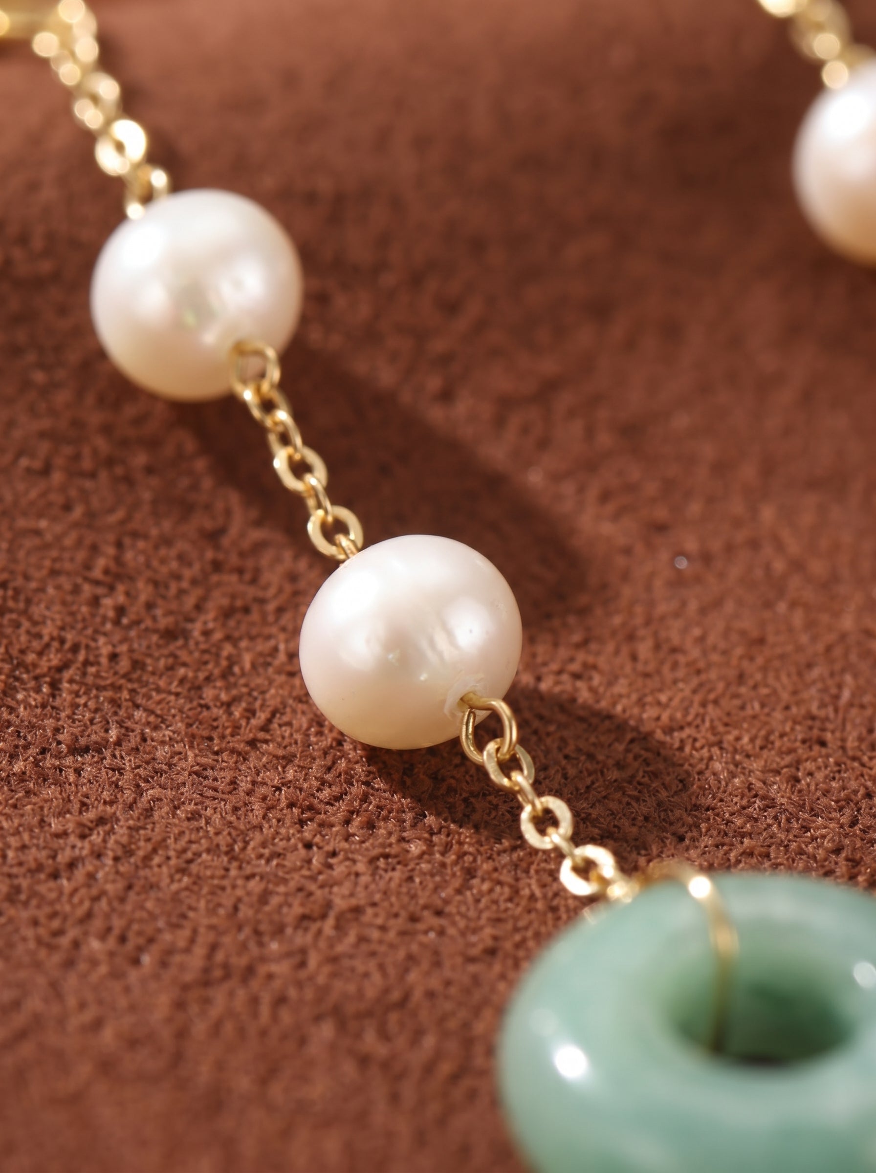 Close-up of Dewdrop Freshwater Pearl Ring Dangle Earrings featuring two white seed pearls strung on a delicate gold chain, with a smooth, polished green jade ring dangling at the bottom. @pearl
