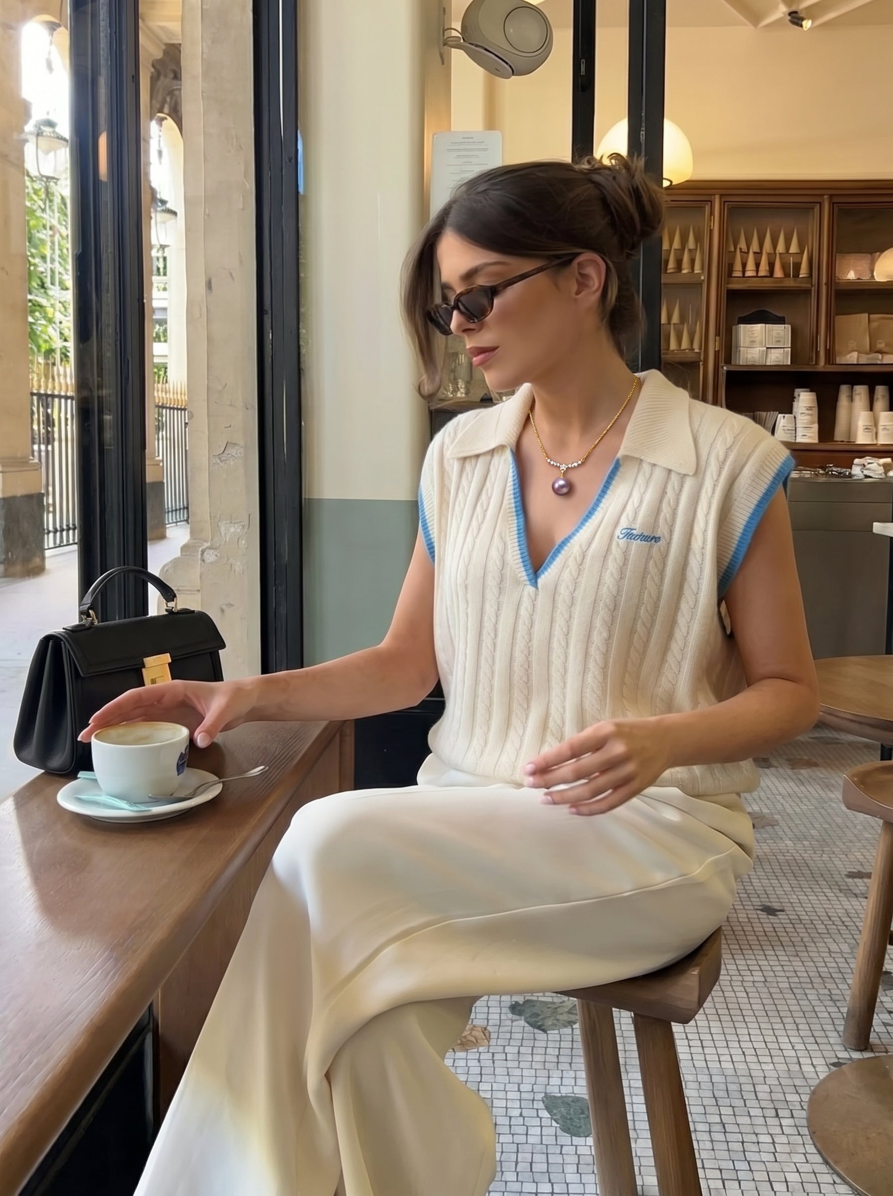 Une femme portant le collier pendentif en grappe d'étoiles Eclat en perle d'eau douce avec une perle violette, assise à une table de café avec une tasse de café. @lifestyle