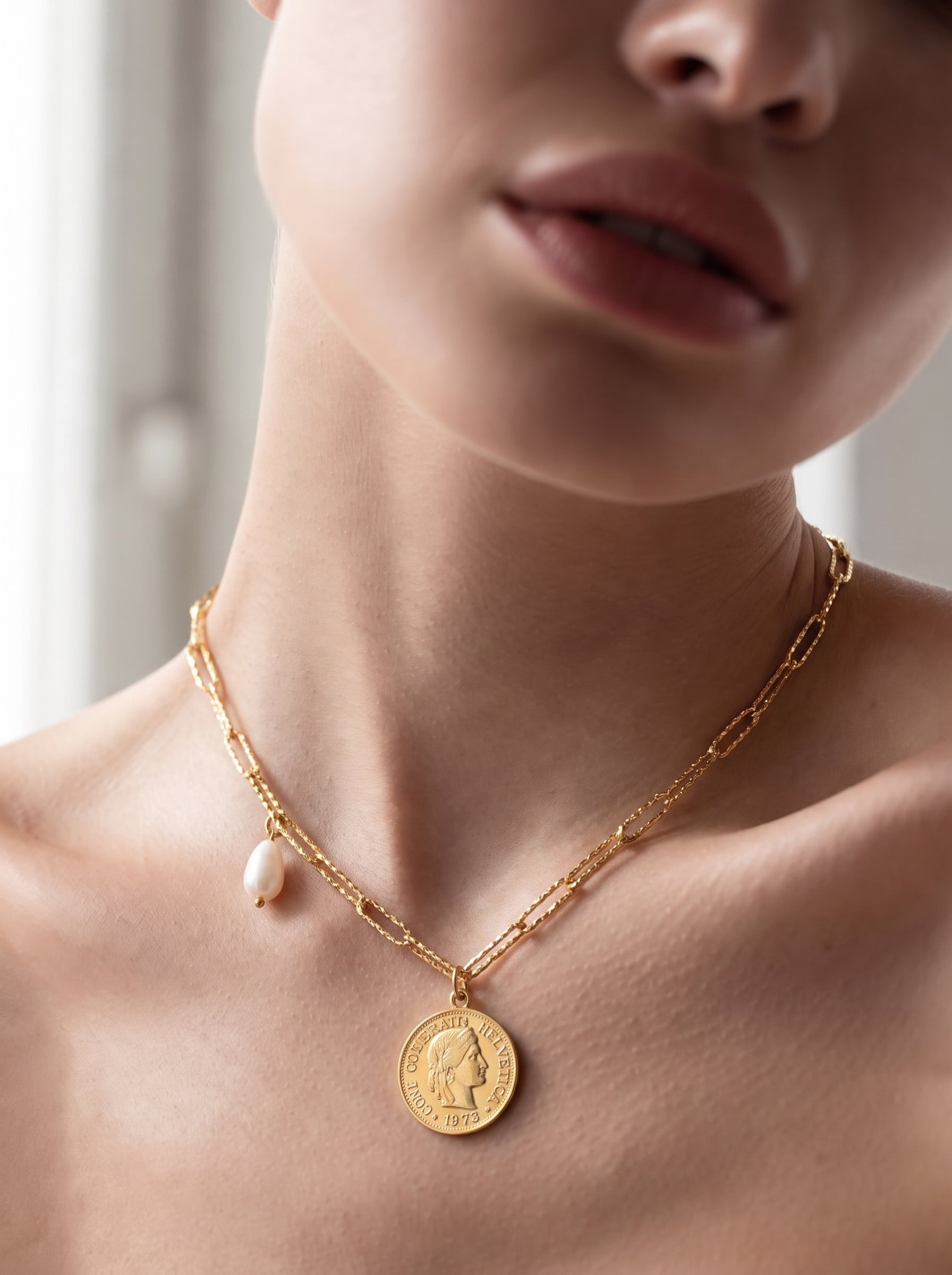 Gros plan d'un collier à chaîne imposante dorée avec un pendentif pièce et un seul accent en perle blanche d'eau douce, porté par une femme. @model