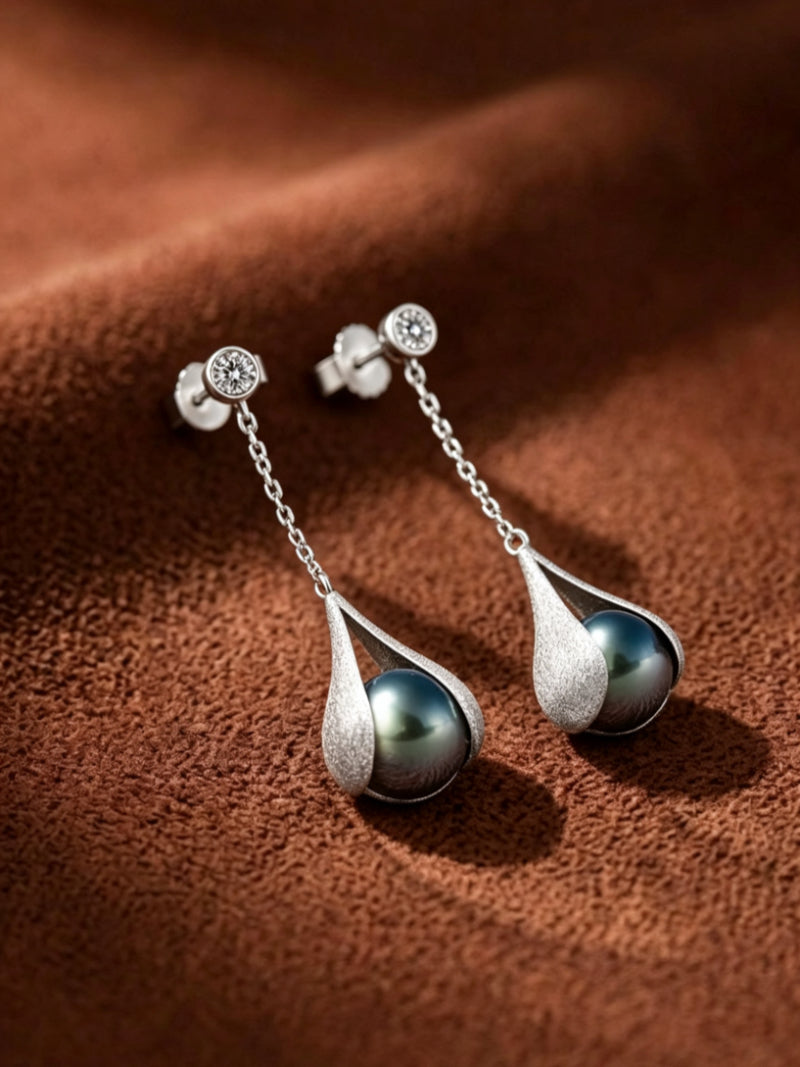 Enfold Tahitian pearl drop earrings featuring a 10mm round black pearl suspended in a textured silver-tone teardrop setting with a clear stone stud.