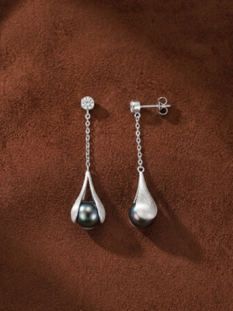 Enfold Tahitian pearl drop earrings with clear stone studs and textured silver-tone settings on a brown background.