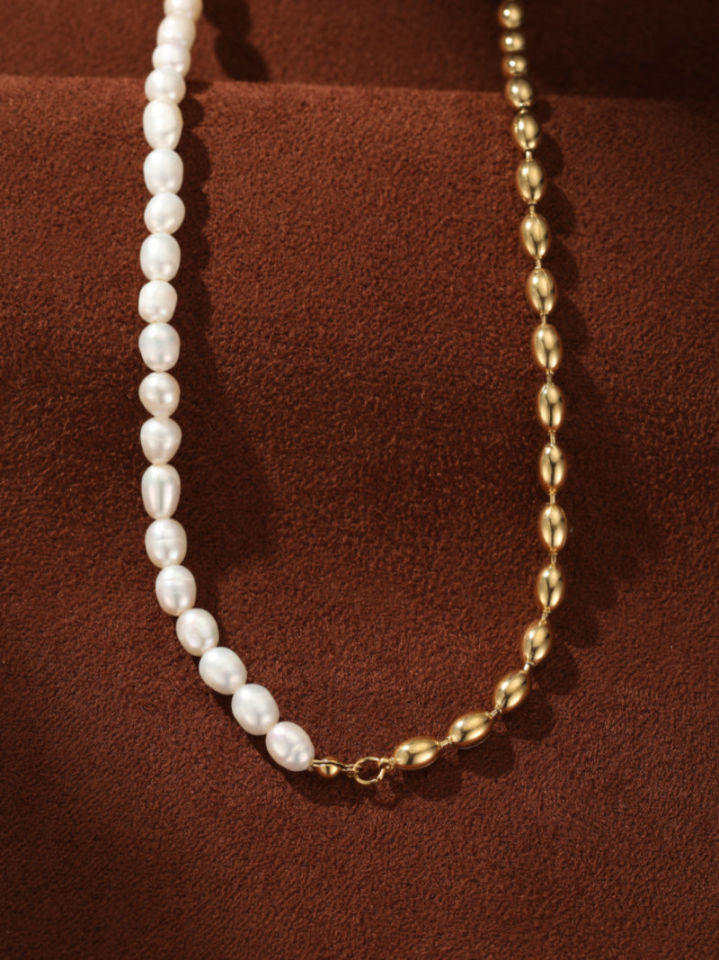 A split necklace featuring lustrous white freshwater seed pearls on one side and a polished gold-toned oval link chain on the other, displayed on a textured brown surface.