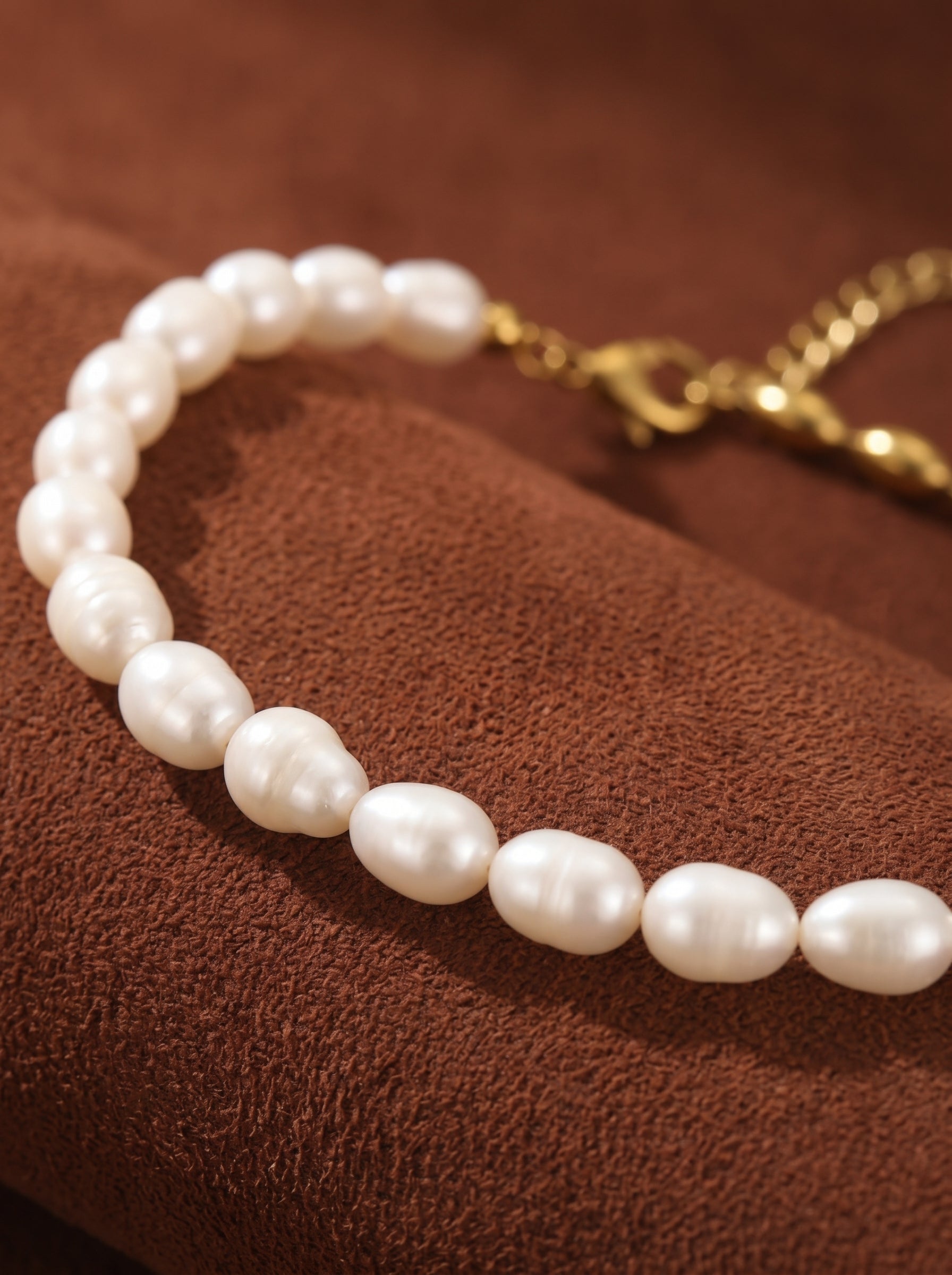 A close-up of the Equilibrium necklace, showcasing a split design with lustrous white freshwater seed pearls on one side and a gleaming gold-toned chain on the other, resting on a rich brown textured surface. @pearl