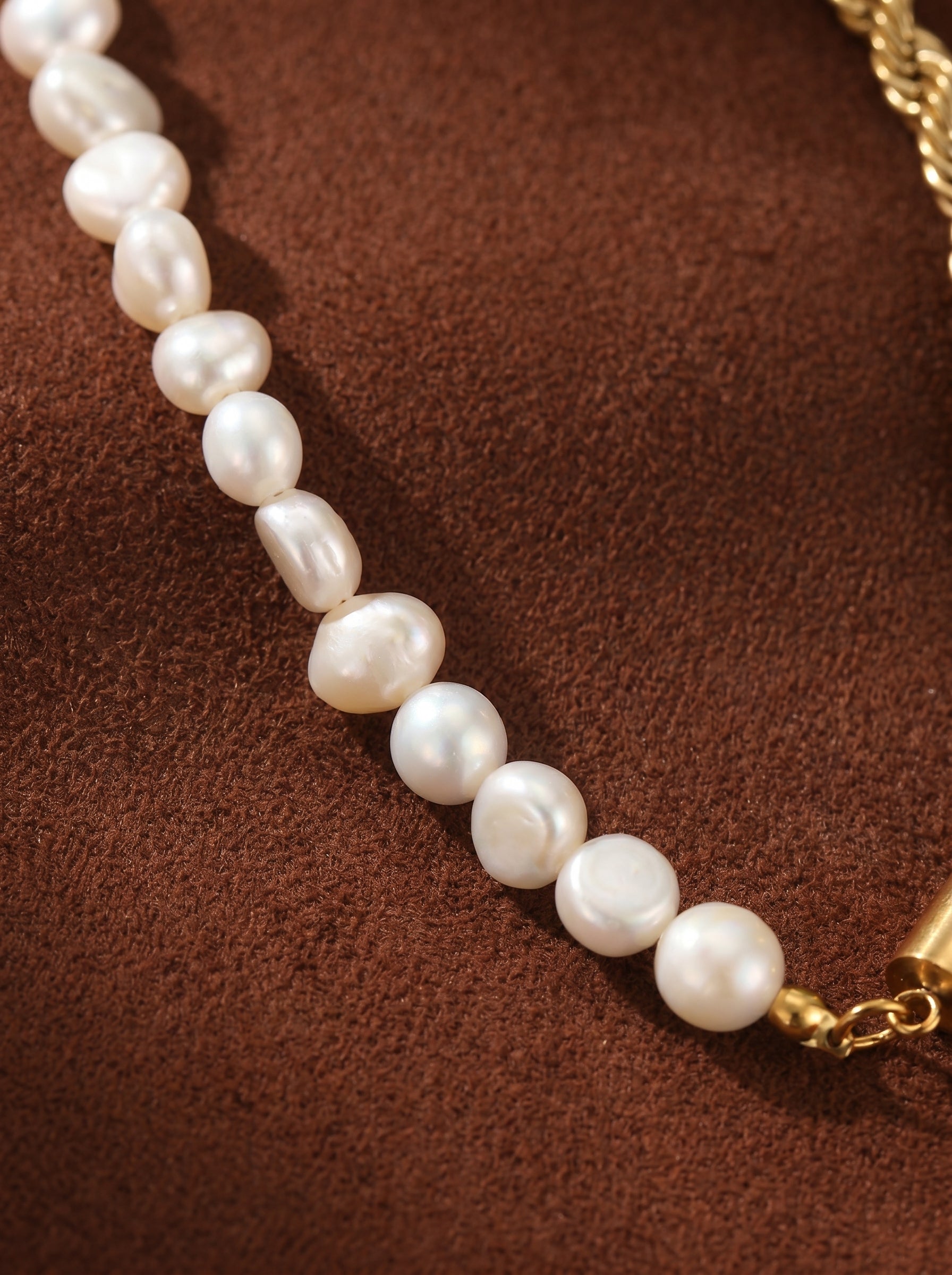 Close-up of a white freshwater pearl beaded necklace with a gold chain accent against a brown textured background. The pearls are irregular in shape and vary in size, showcasing their natural beauty. The gold chain adds a modern contrast to the classic pearls. @pearl