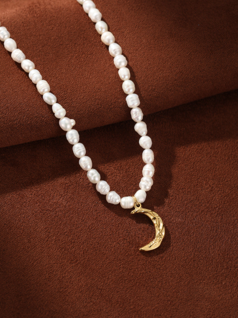 Ethereal Gleam choker necklace featuring a strand of irregular white freshwater pearls and a textured golden crescent moon pendant, displayed on a textured brown background.