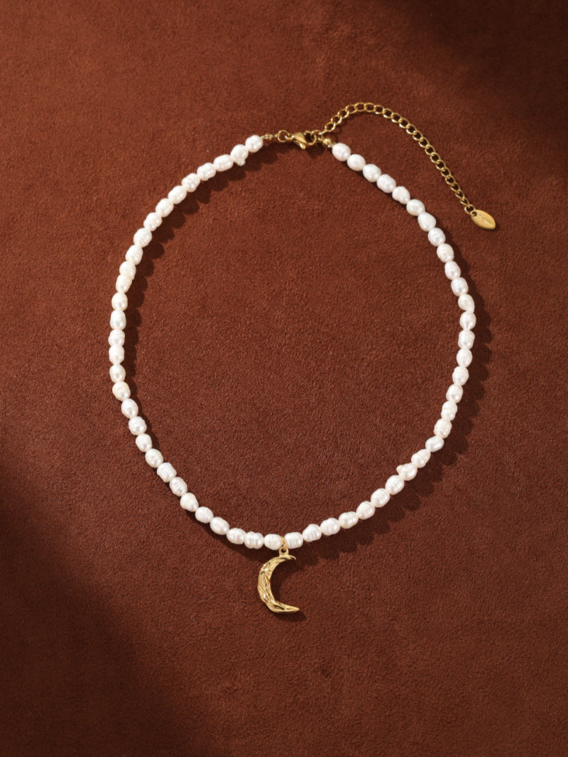 Ethereal Gleam choker necklace with small, irregular freshwater pearls and a textured golden crescent moon pendant on a brown background. @pearl