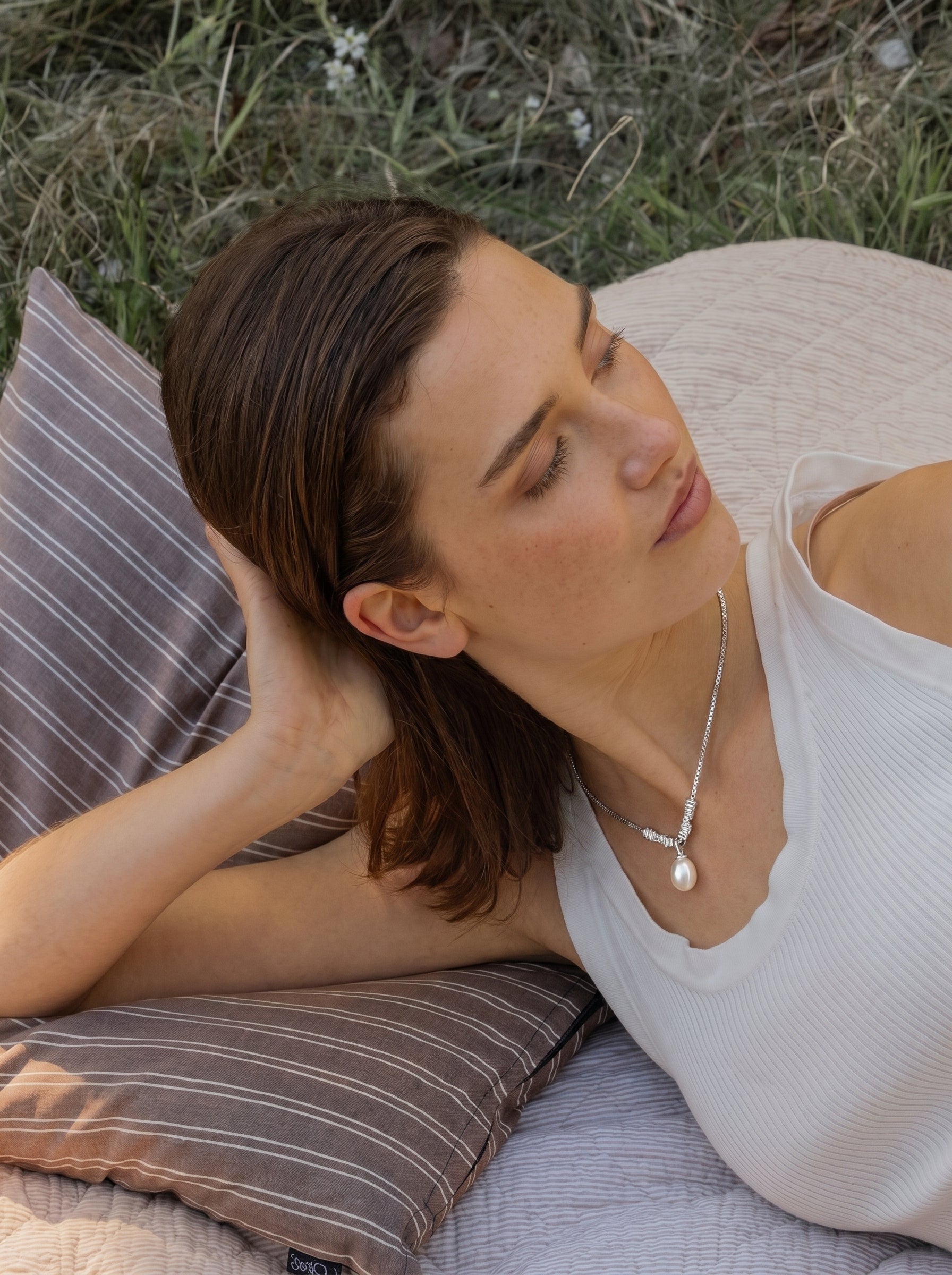 Une femme portant le collier pendentif à chaîne Facet en perle d'eau douce à l'extérieur sur une couverture avec des coussins et de l'herbe en arrière-plan. @lifestyle