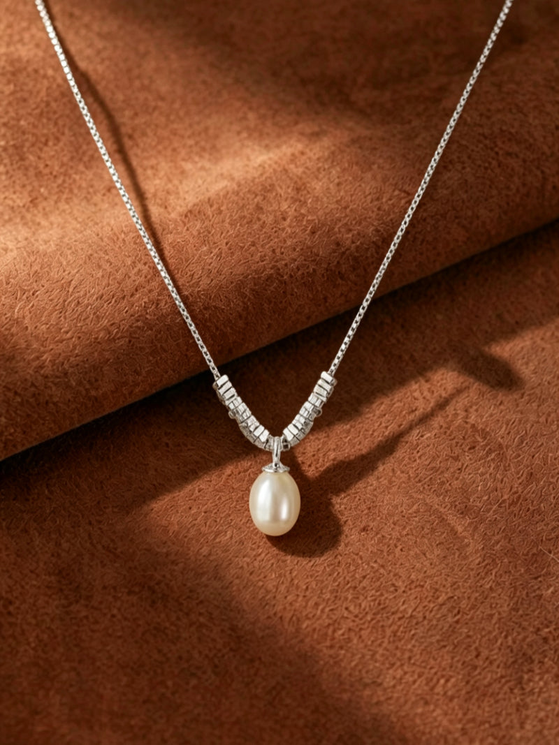A close-up of the Facet Freshwater Pearl Chain Drop Necklace, featuring a delicate silver-toned chain with segmented architectural accents leading to a single, luminous 9mm white drop-shaped freshwater pearl.