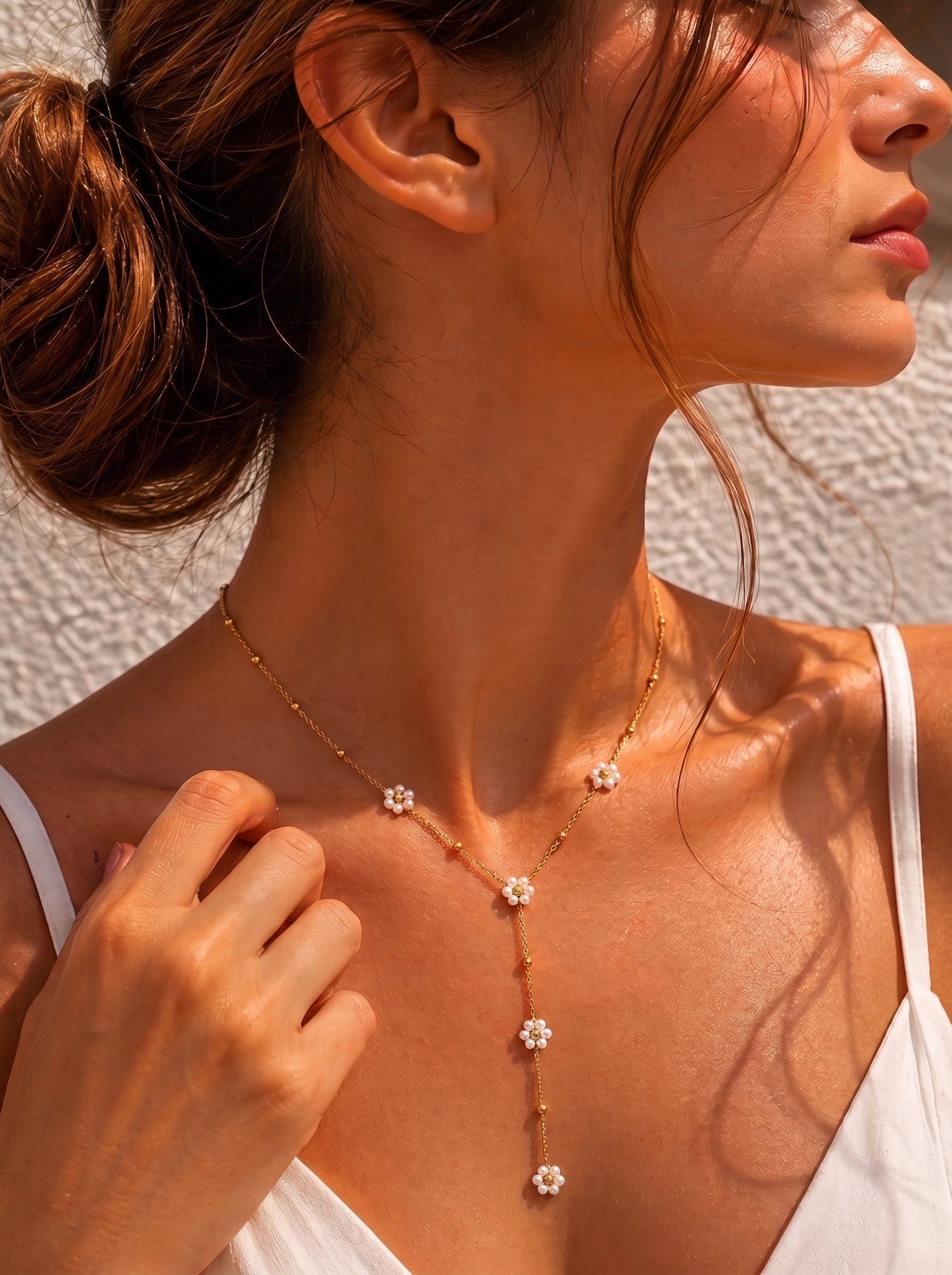 A woman wears a delicate gold layered necklace with small white pearl flowers cascading down her décolletage. @model