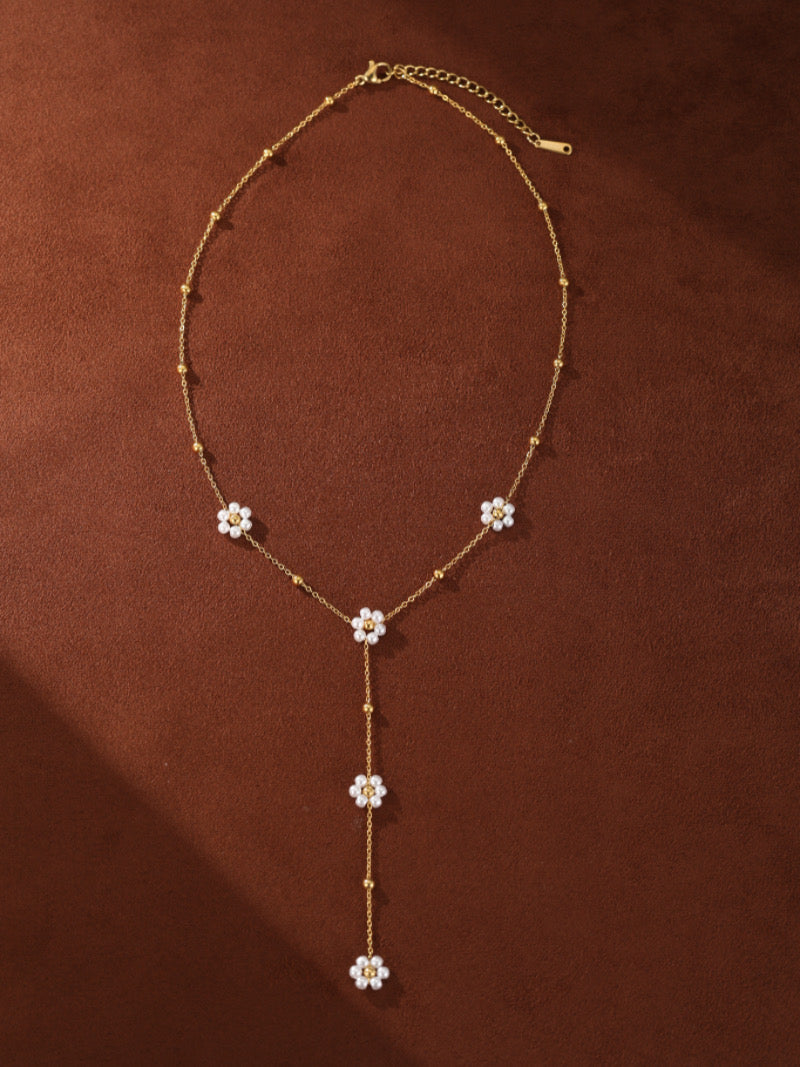 Gold layered necklace with small beaded chains and five flower charms, each centered with a tiny white pearl.
