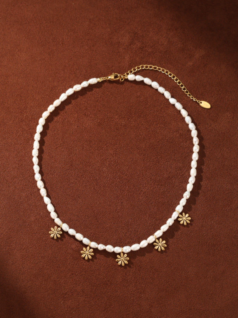 Gemma Strand choker necklace with small white freshwater pearls and gold flower charms on a brown background @pearl
