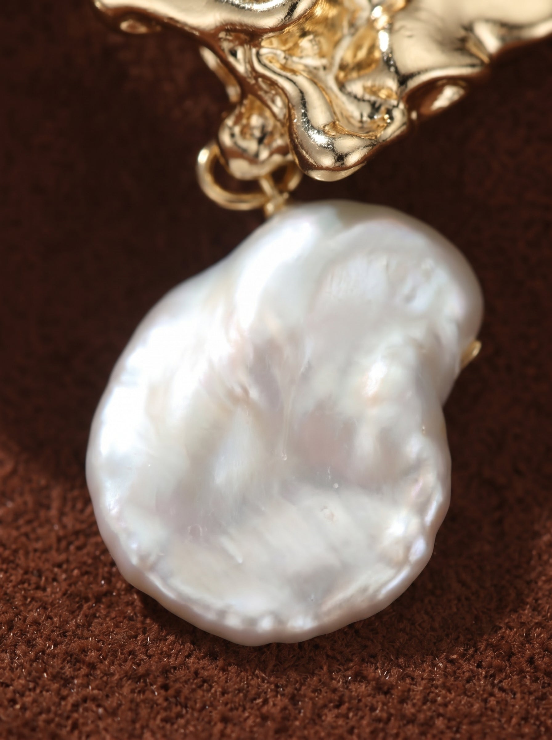Close-up of a Gilded Ember earring featuring a large, irregularly shaped white baroque pearl suspended from an organic gold-toned stud.@pearl