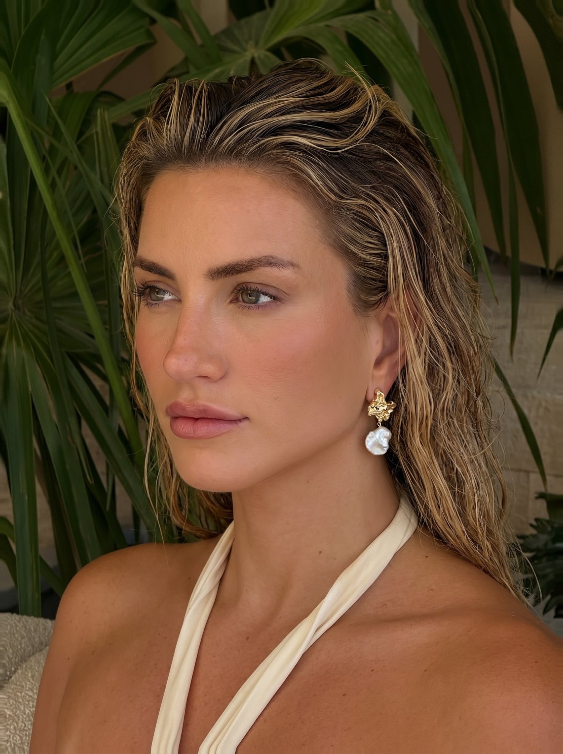 Gilded Wave Freshwater Pearl Drop Earrings feature a gold-toned textured top with a large, irregular white Keshi pearl dangling below, worn by a woman with wet hair against a backdrop of lush green foliage. @lifestyle #lifestyle